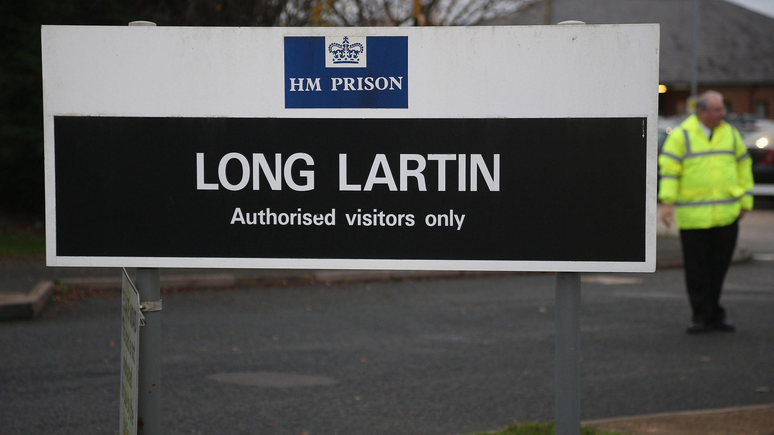 A sign for Long Lartin outside the prison reads "authorised visitors only". A man is nearby in a high-vis jacket.