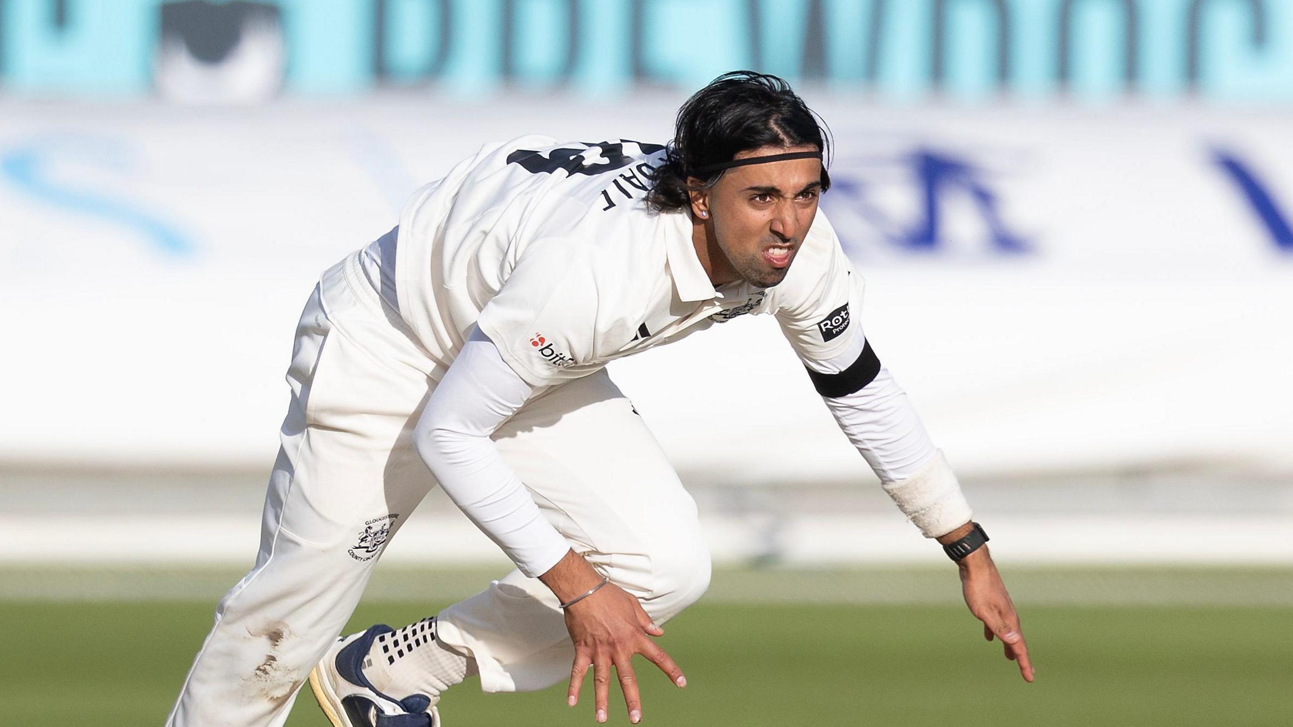 Ajeet Singh Dale has his body almost bent double through the exertion of bowling fast. He is also wearing a black watch on his left arm and he has a headband to keep his black flowing hair in check.