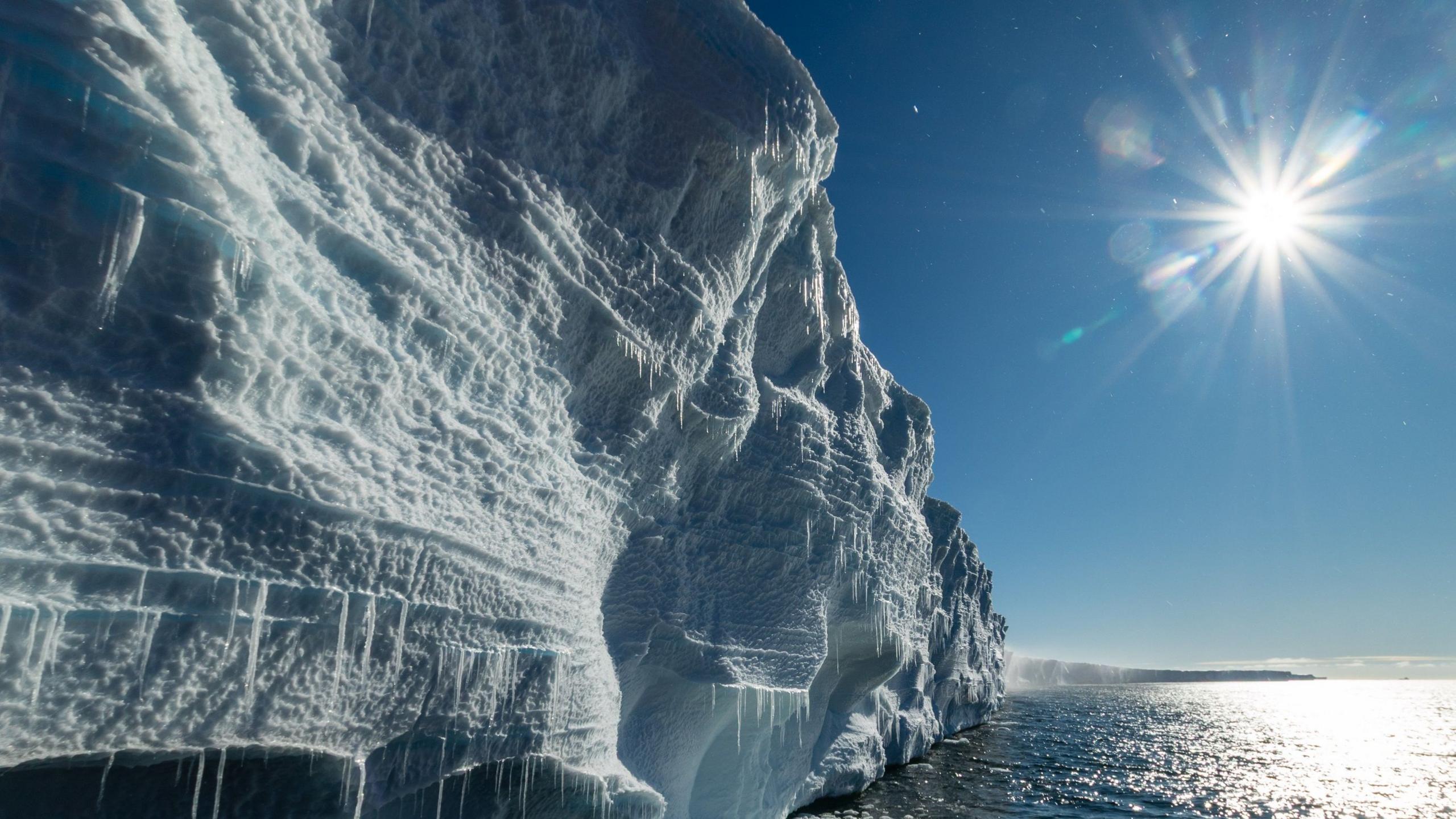 A close-up shot of a large ice mass. On the right-hand side is open ocean and a blue sunny sky.