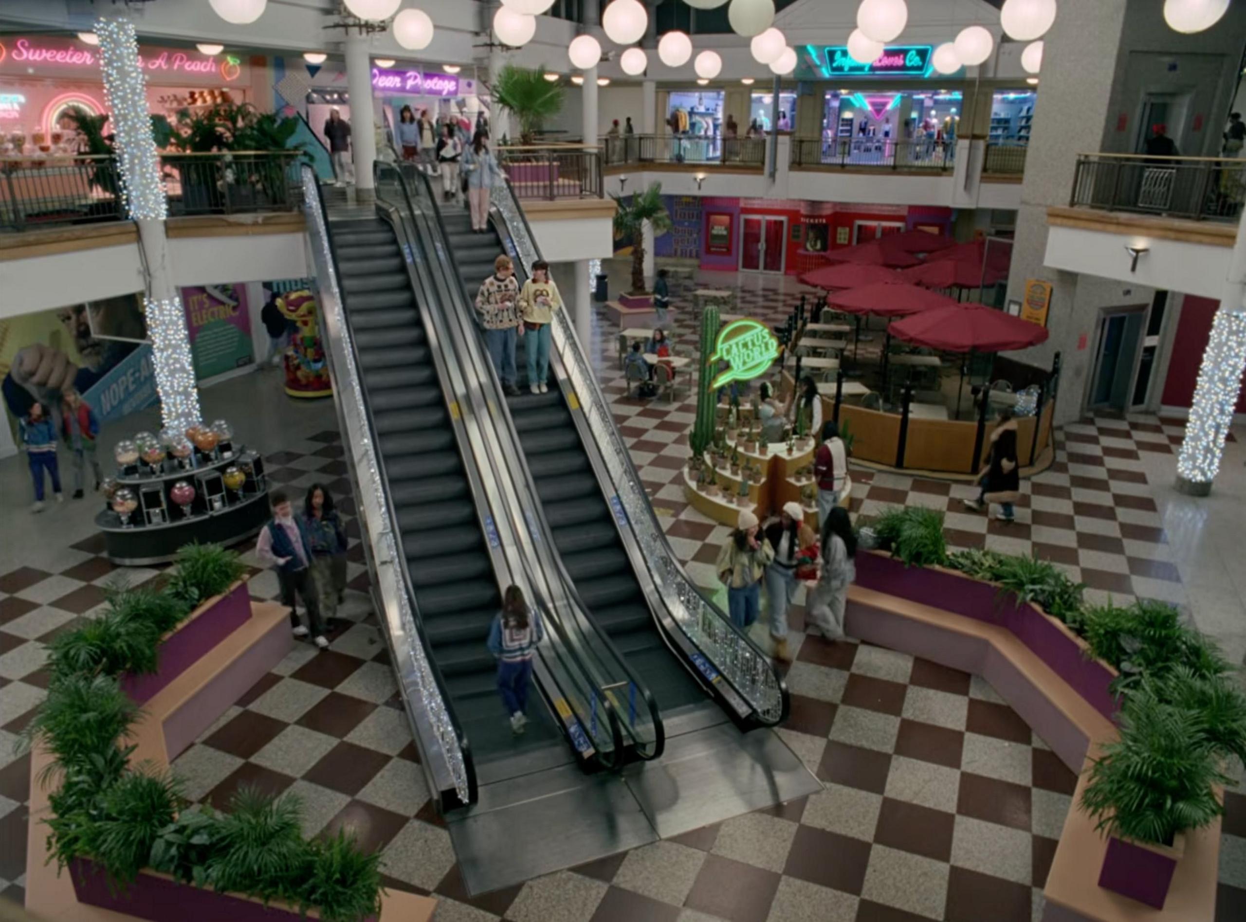 A still from the official music video for “Opalite" by Taylor Swift. It shows Taylor and famous Hollywood actor Domhnall Gleeson going down the escalators of Croydon's The Whitgift Centre. The shopping centre has been decorated to look as if it's from the 1980s. 