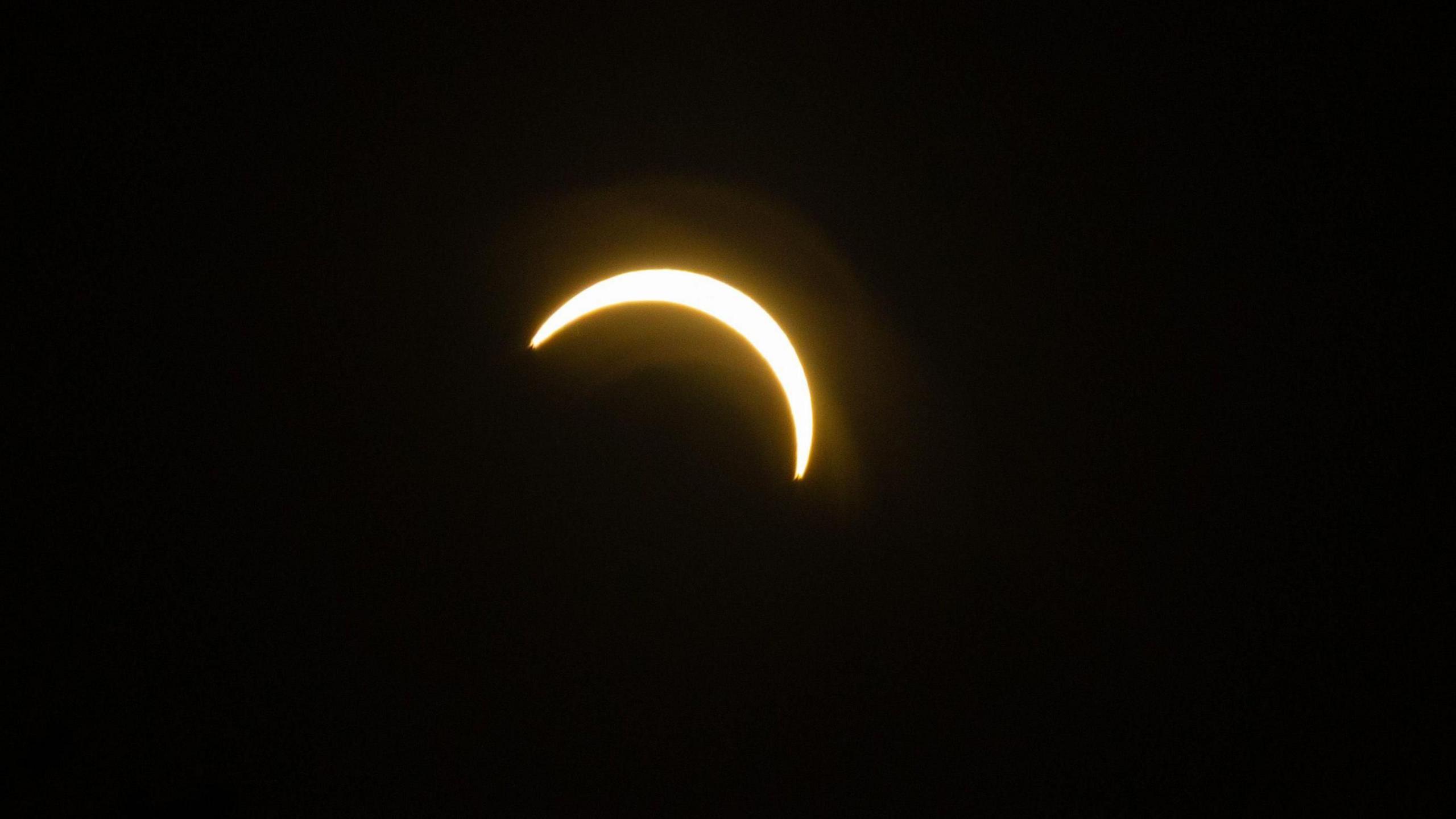 A bright crescent of sunlight appears against a black sky as the Moon passes in front of the Sun during a partial solar eclipse.