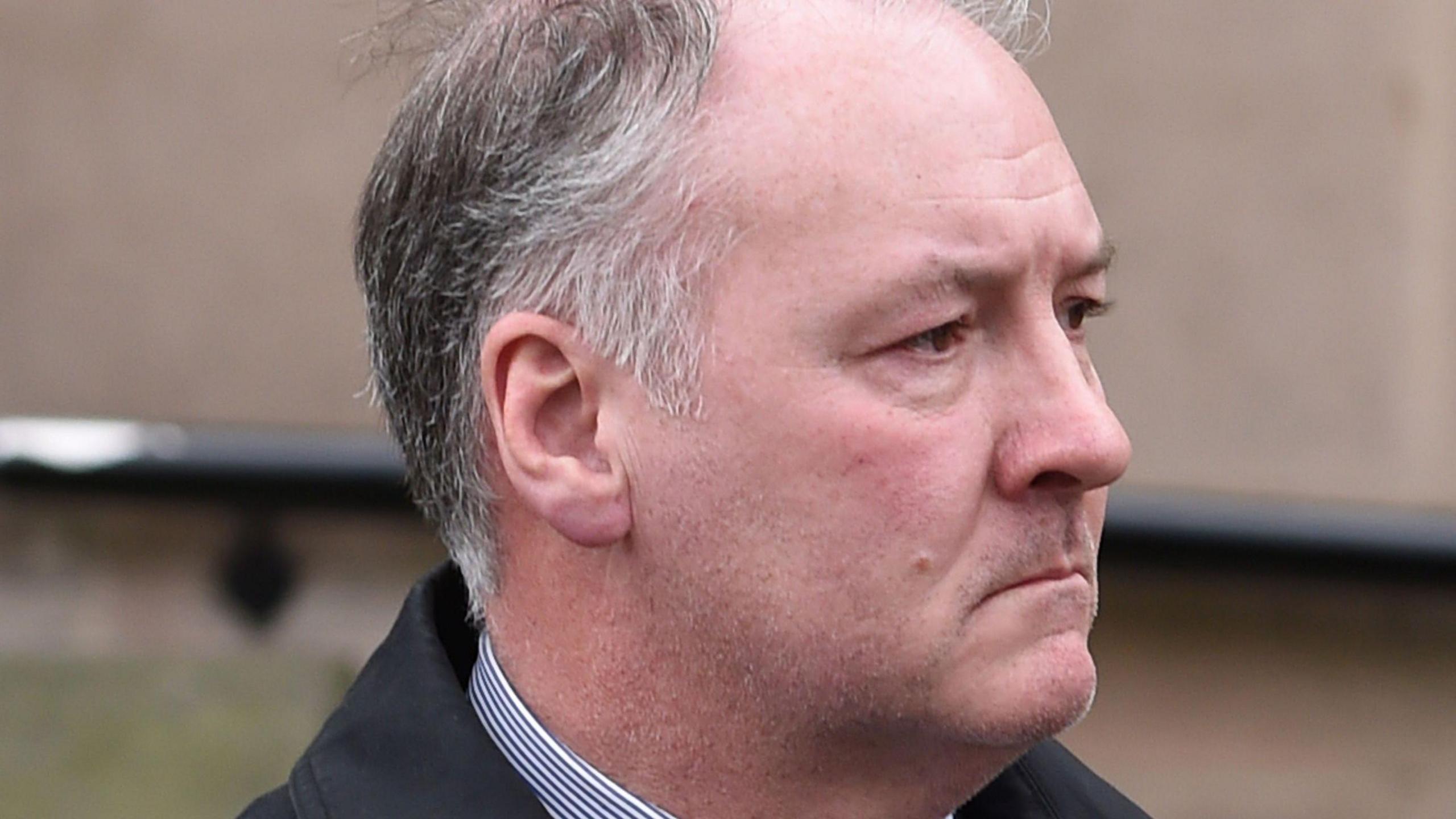 A man with grey hair and a white shirt and dark jacket
