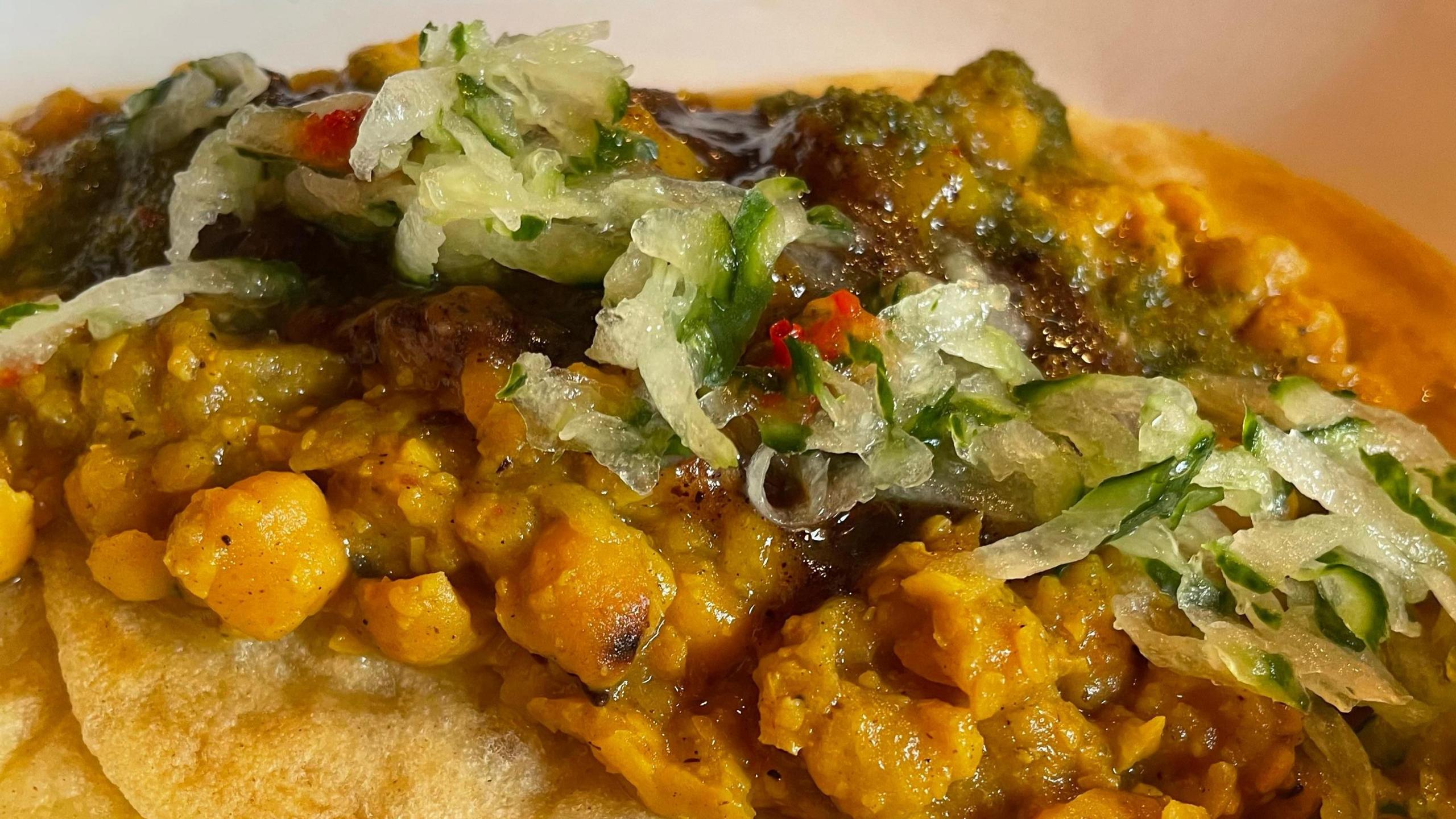 Curried chickpeas served on two fried flatbreads with shredded cucumber of top.