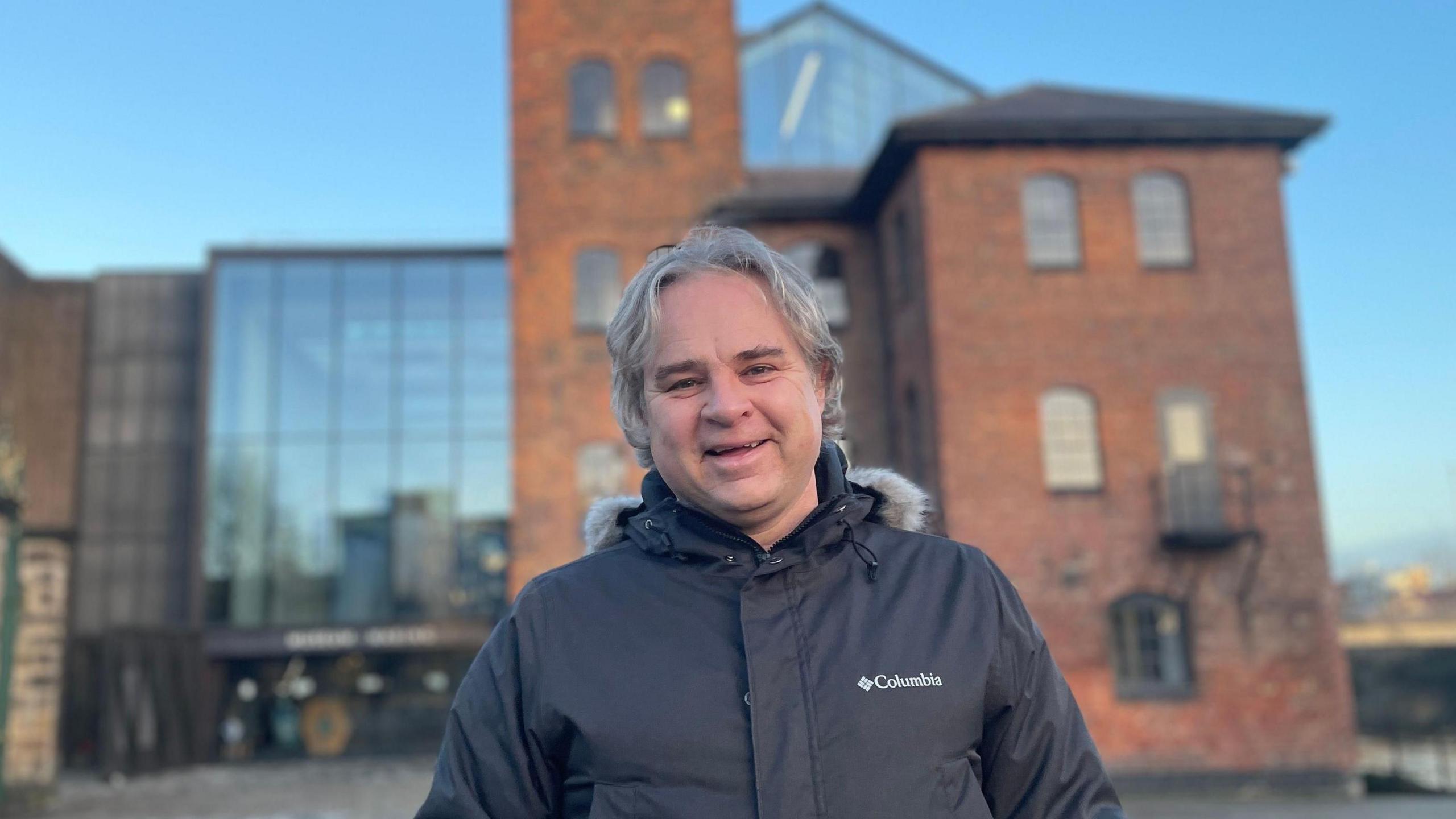 Man stands in front of a museum in a black coat and smiling at the camera