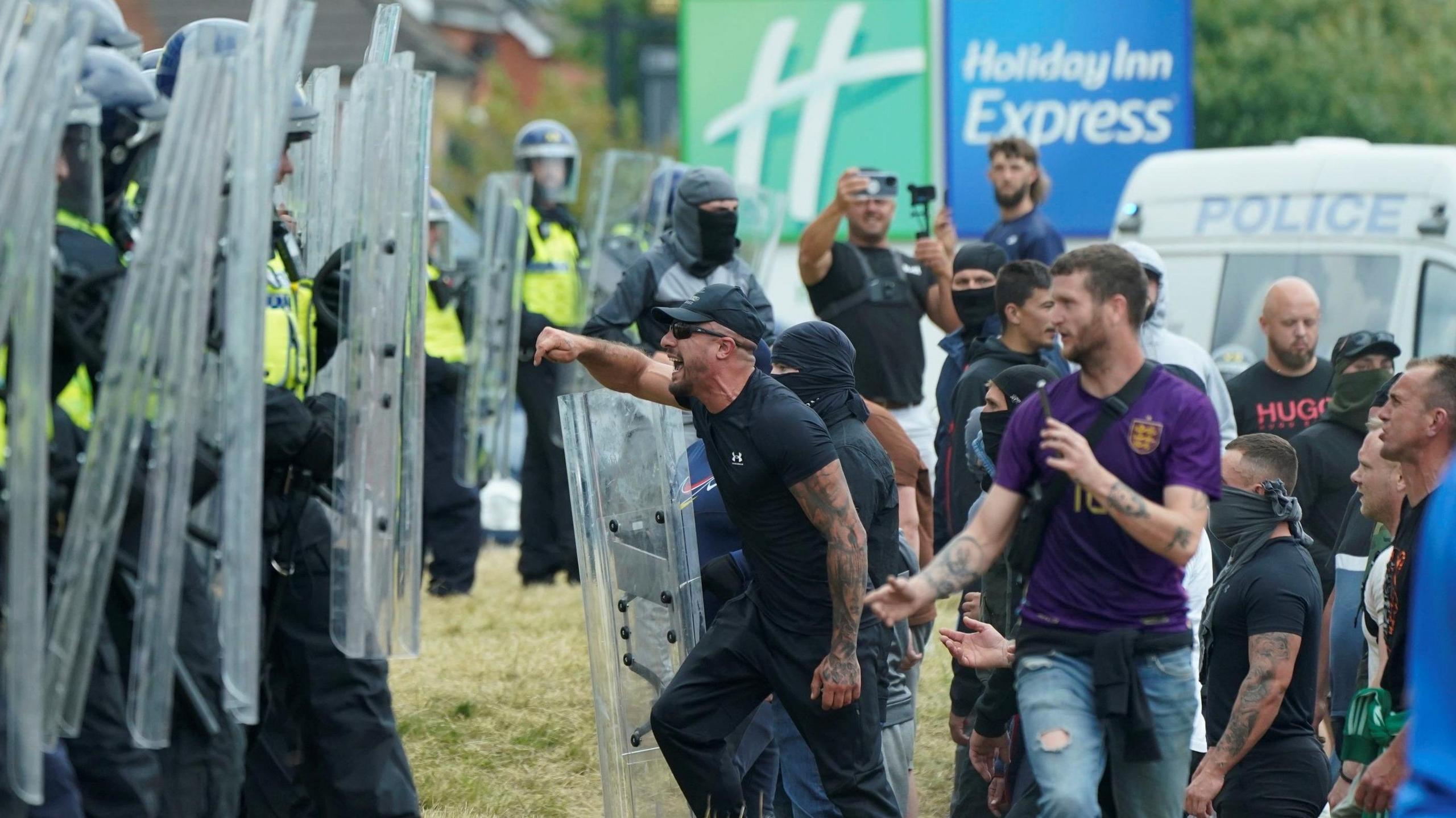 A man yells at a line of police officers with shields