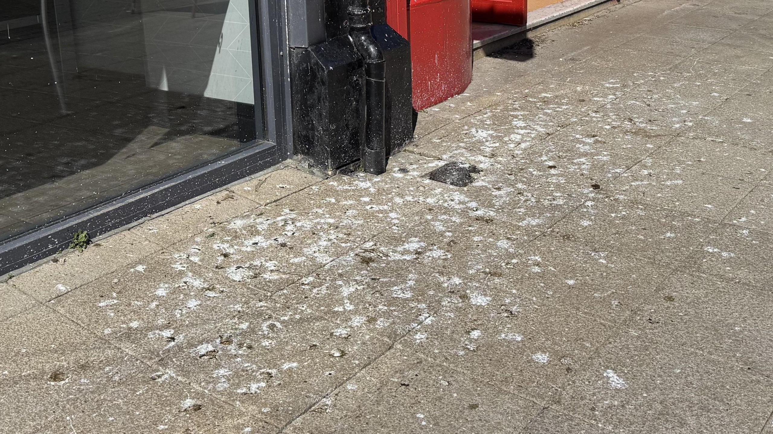 A part of a pavement outside a shop covered in bird poo