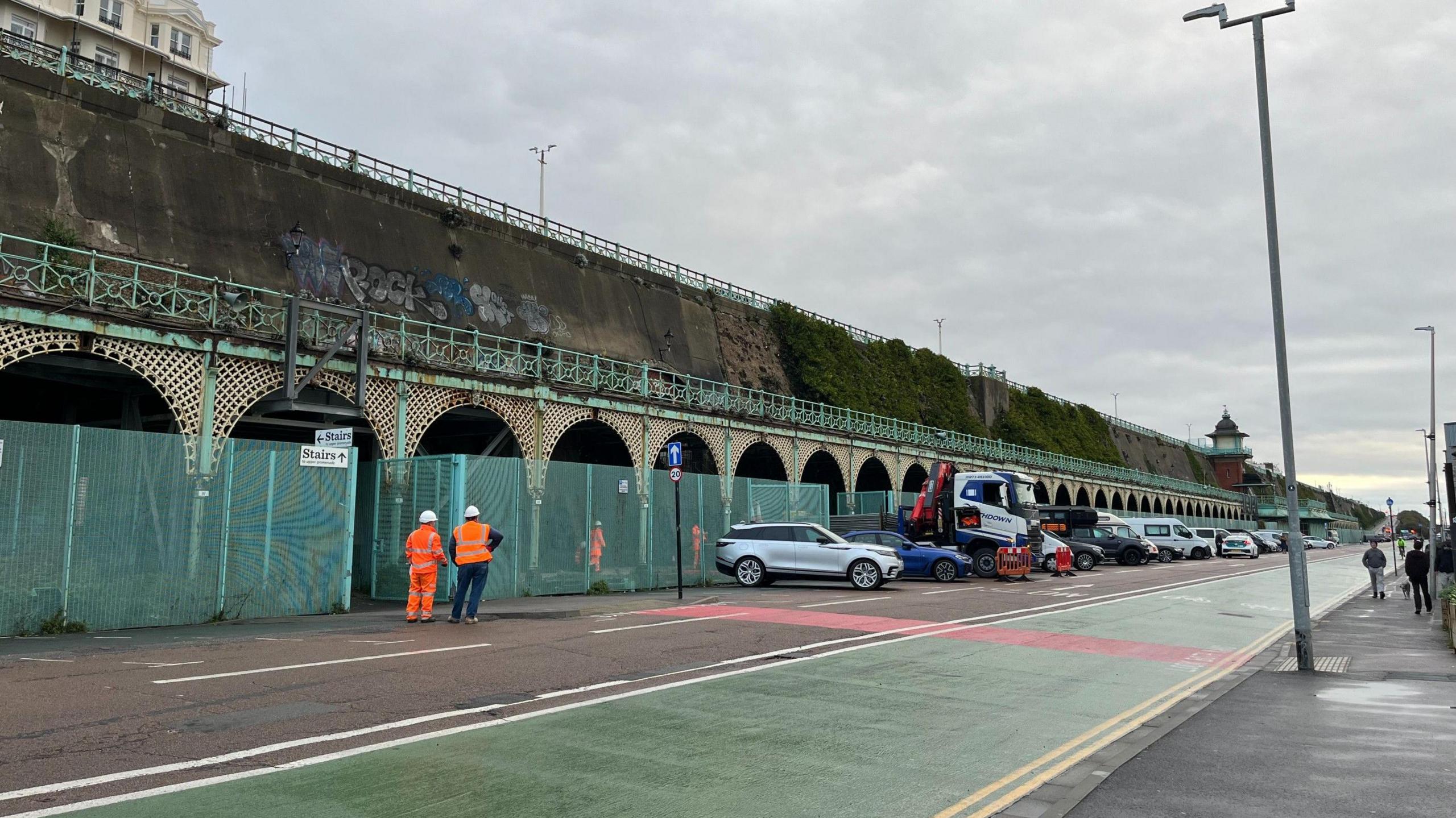 Two workers in hi vis stand looking at Madeira Terrace in Brighton, ahead of maintenance work beginning on Monday