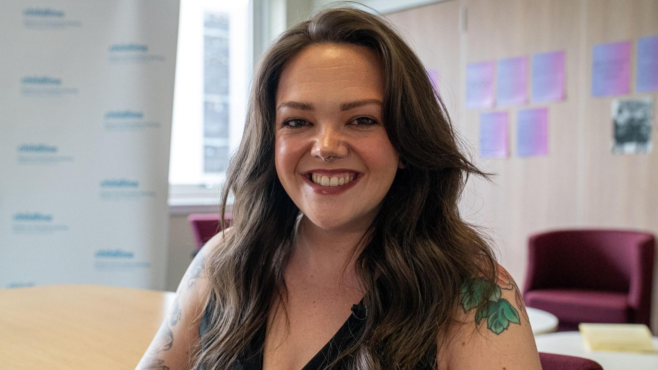 A photo of Lauren Burke looking straight at the camera. She is indoors in some kind of office. She has long brown hair.