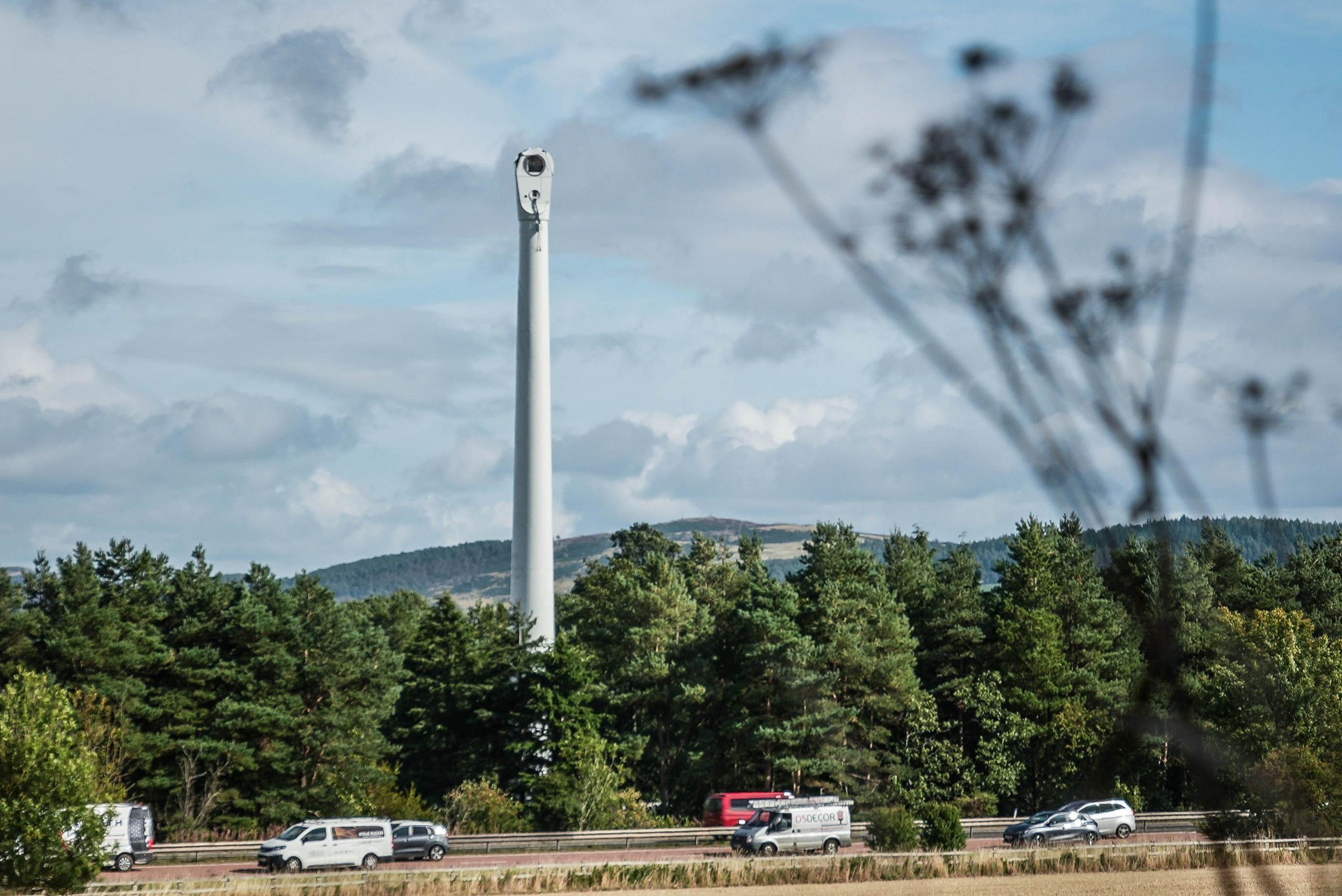 The remains of a wind turbine in a field with traffic in the foreground