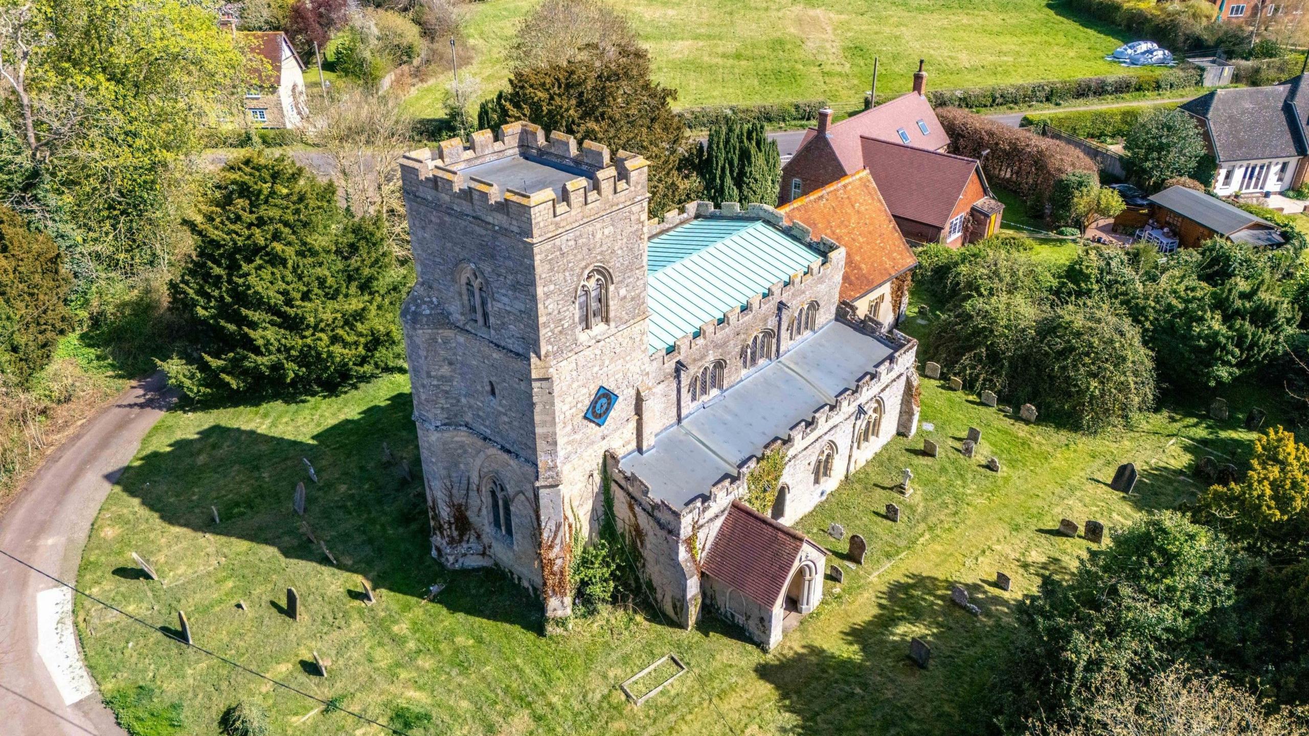 A 12th century stone church seen from above. It is sat in a churchyard surrounded by graves.