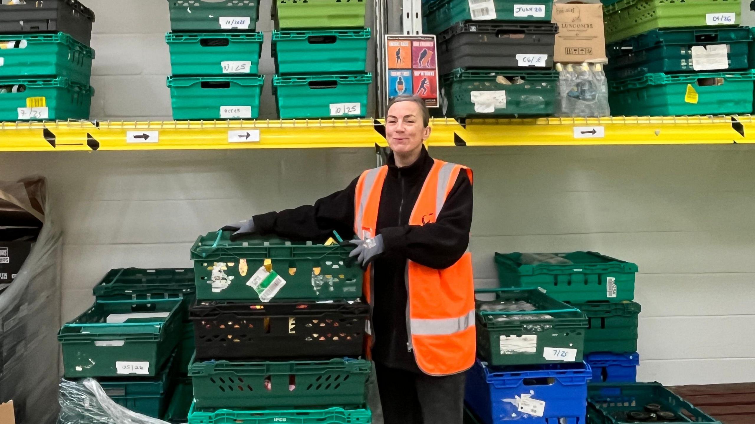 A woman is surrounded by shelves of donated food in a warehouse