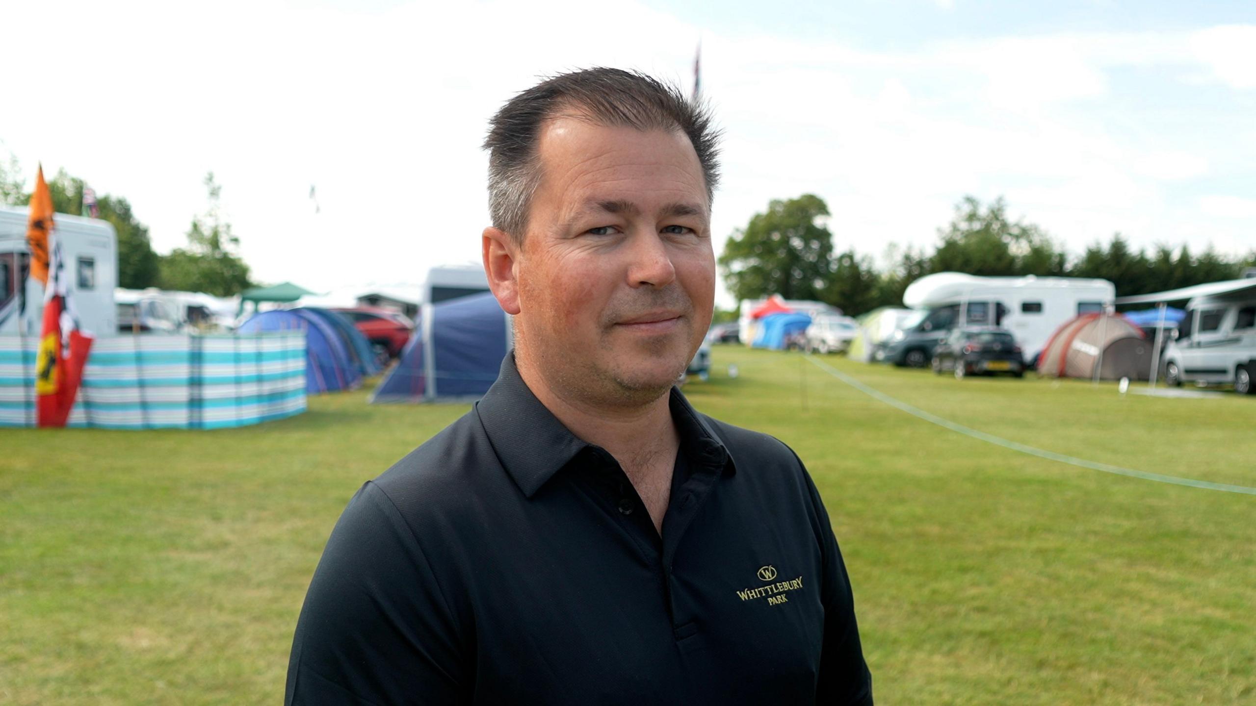 Charles Sargeant managing director at Whittlebury Park, standing in a field at a campsite. He is wearing a dark navy polo top with Whittlebury Park branding.