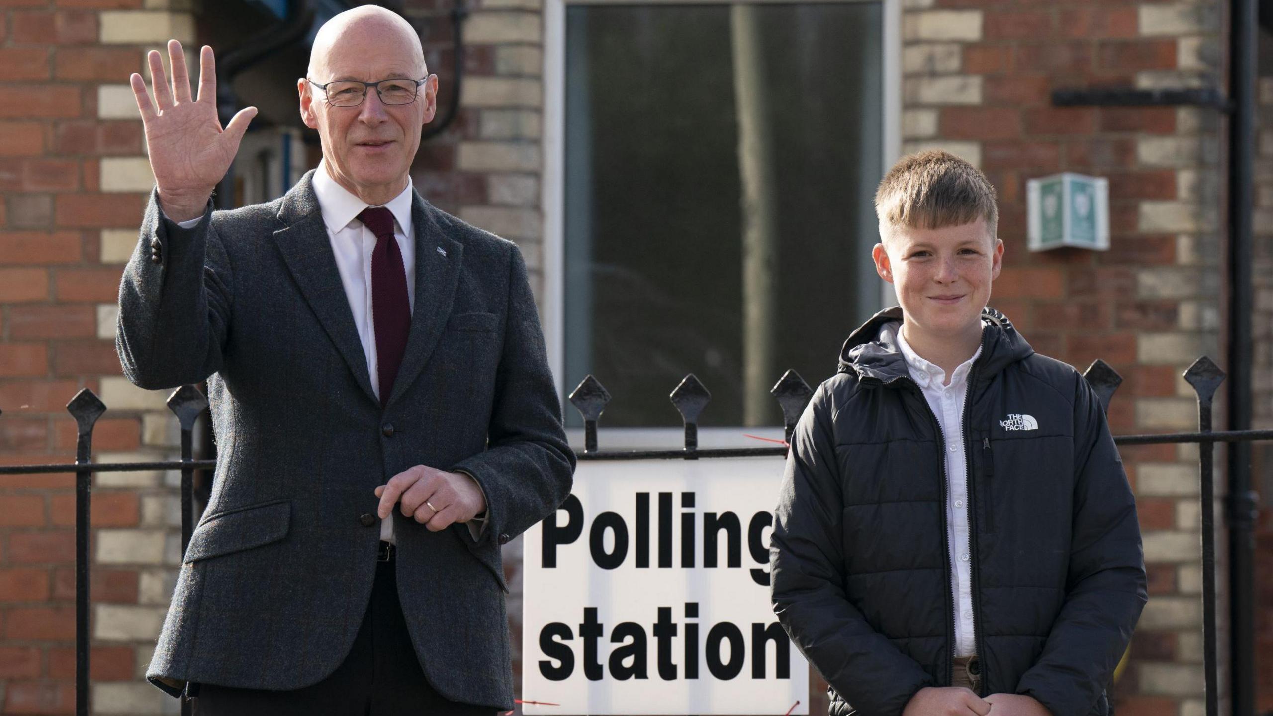 John Swinney waves as he arrives to vote with son Matthew