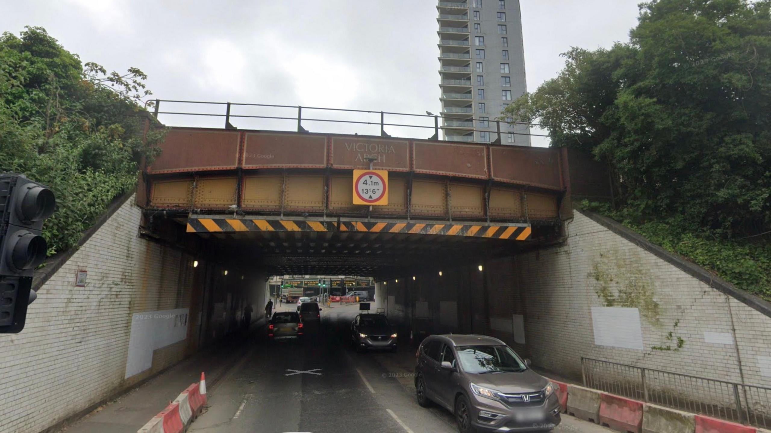 A road running under a brown bridge. The bridge is labelled Victoria Arch and has a height restriction sign attached.