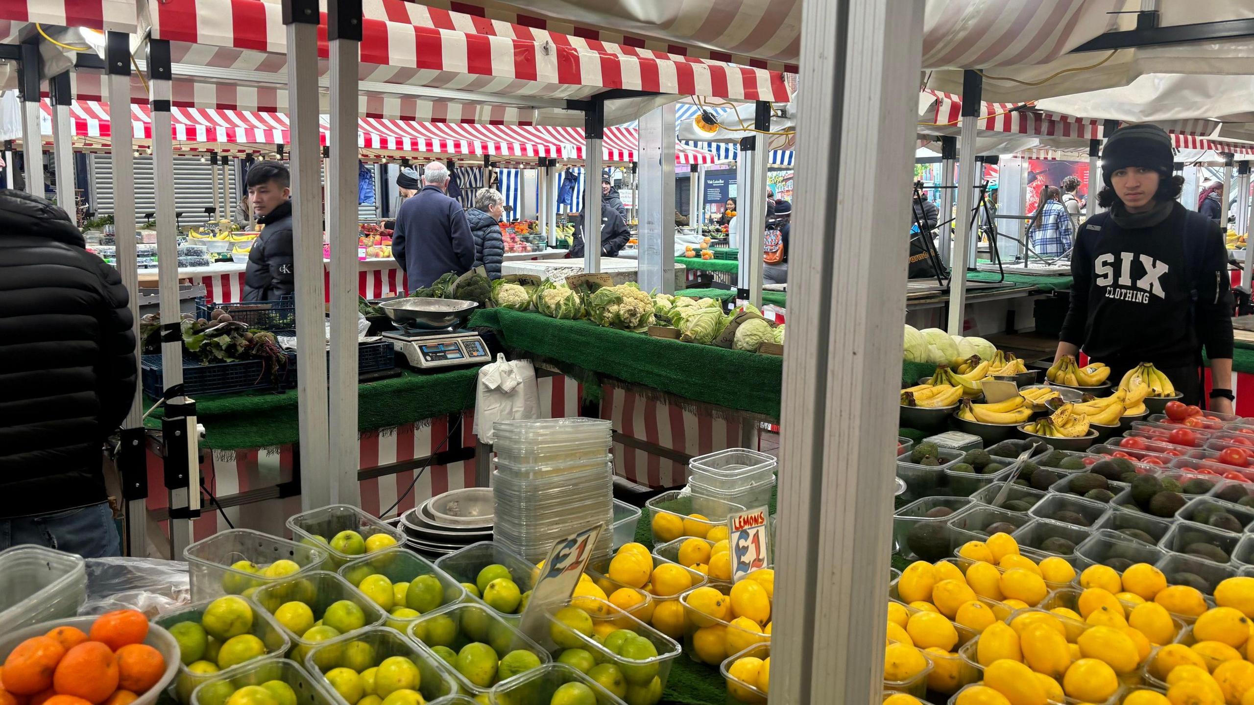 A colourful market stall packed with citrus and other fruit and veg under red and white awnings.