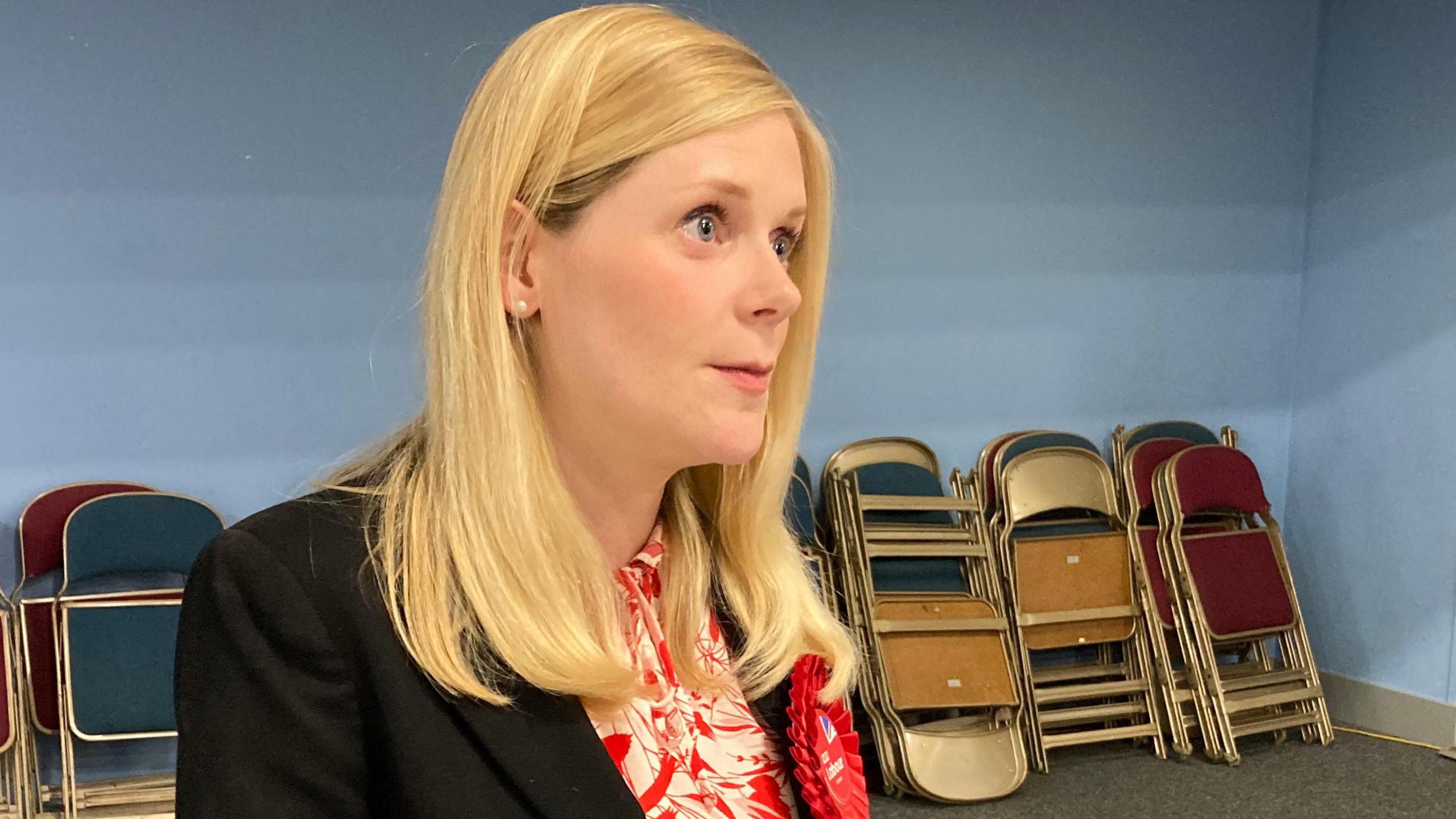 The image is of Labour MP Claire Hazelgrove who is wearing a black blazer and red and white blouse and a Labour red rosette.