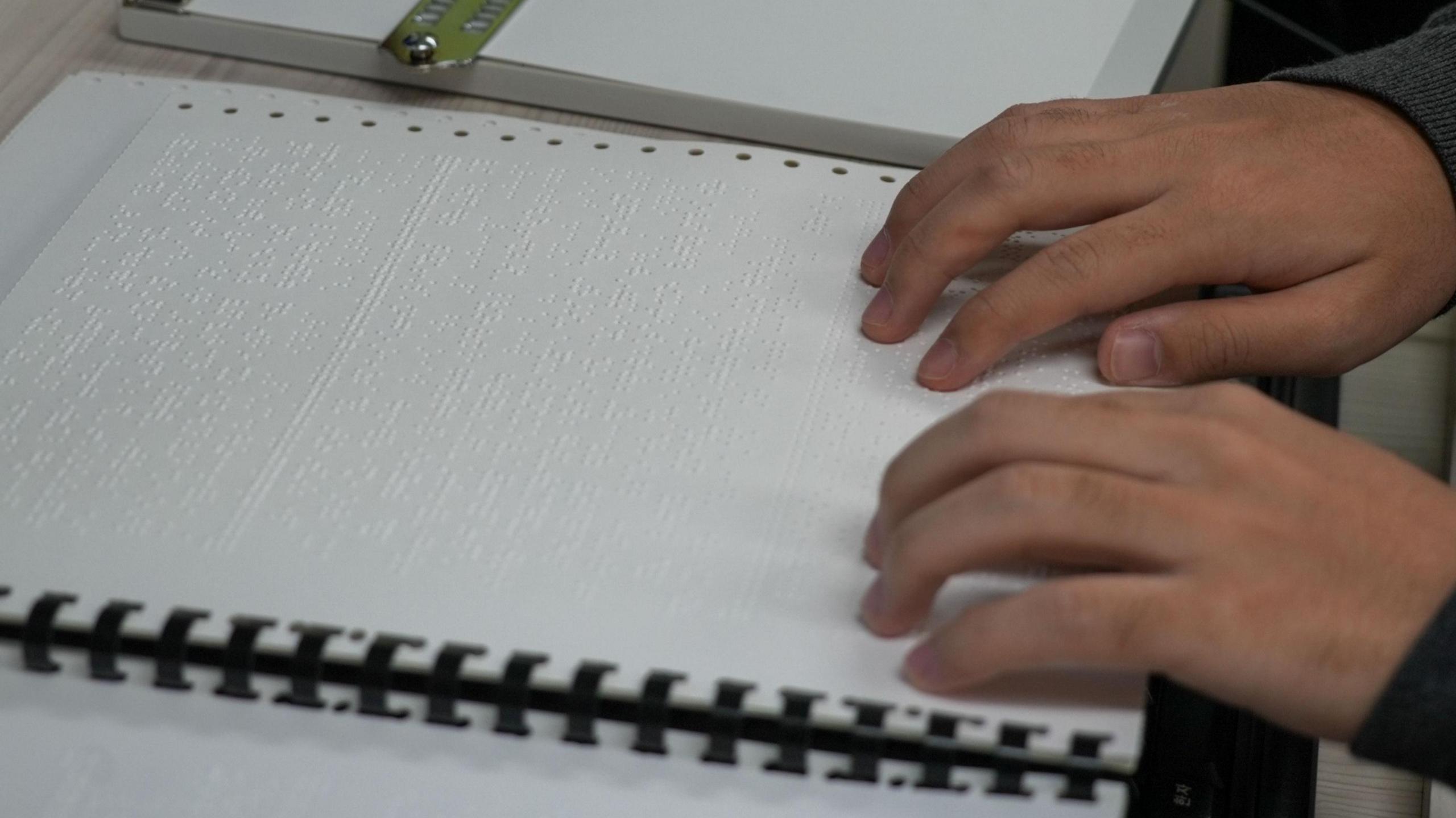 Two hands on a braille practice booklet for the Suneung exam
