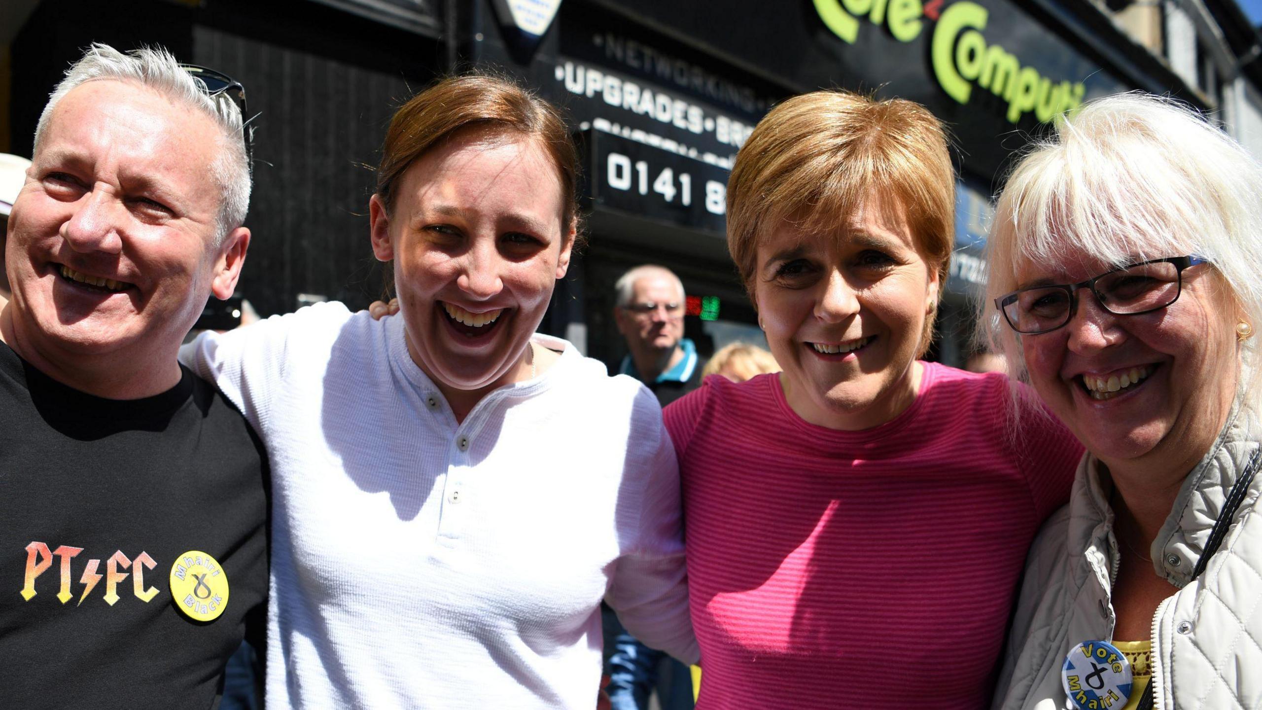 From left to right - Alan Black with silver hair and a black shirt reading PT FC, Mhairi Black in a white top, Nicola  Sturgeon in a pink top and Mhairi Black's mother, who has blond hair, a grey coat and an SNP pin badge  