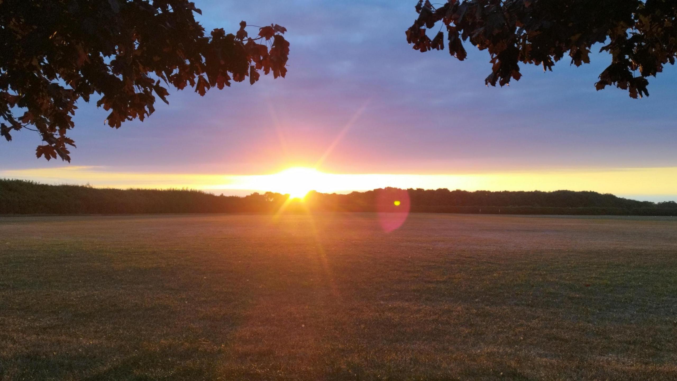 A low sun beams over an empty field.