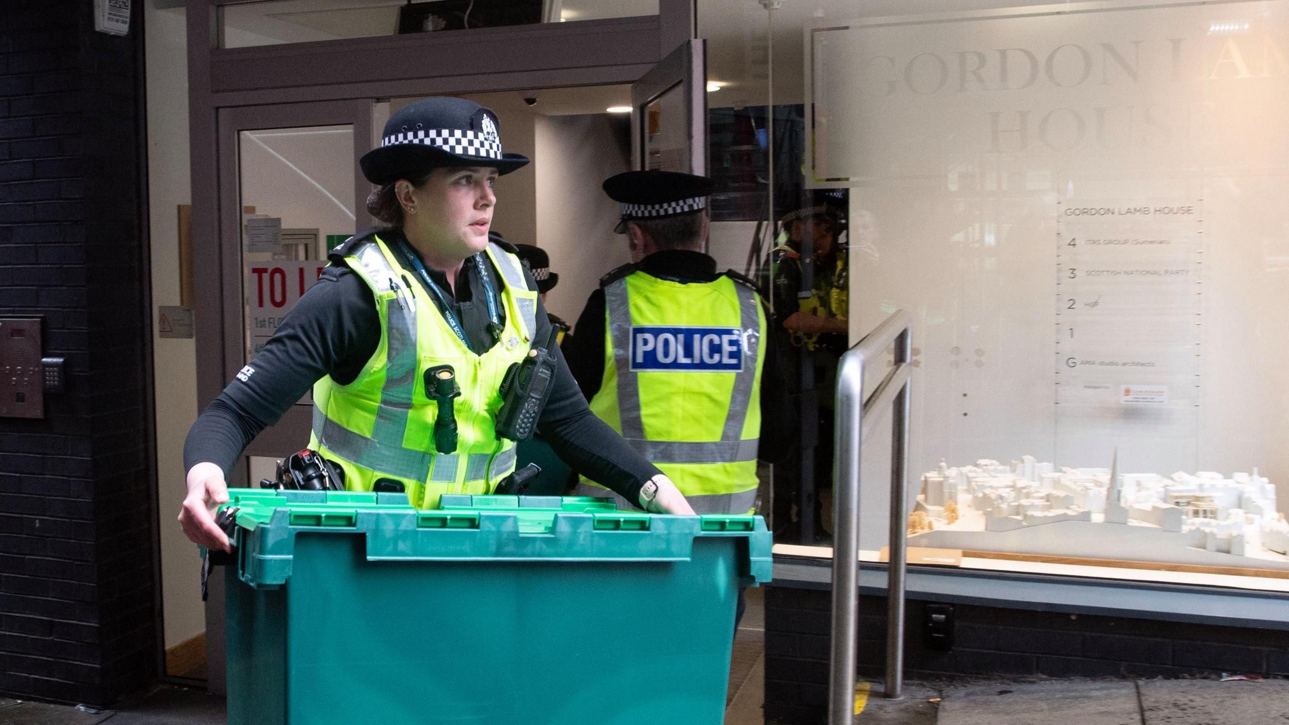 Police officers carrying green crates outside of Gordon Lamb House in Edinburgh.