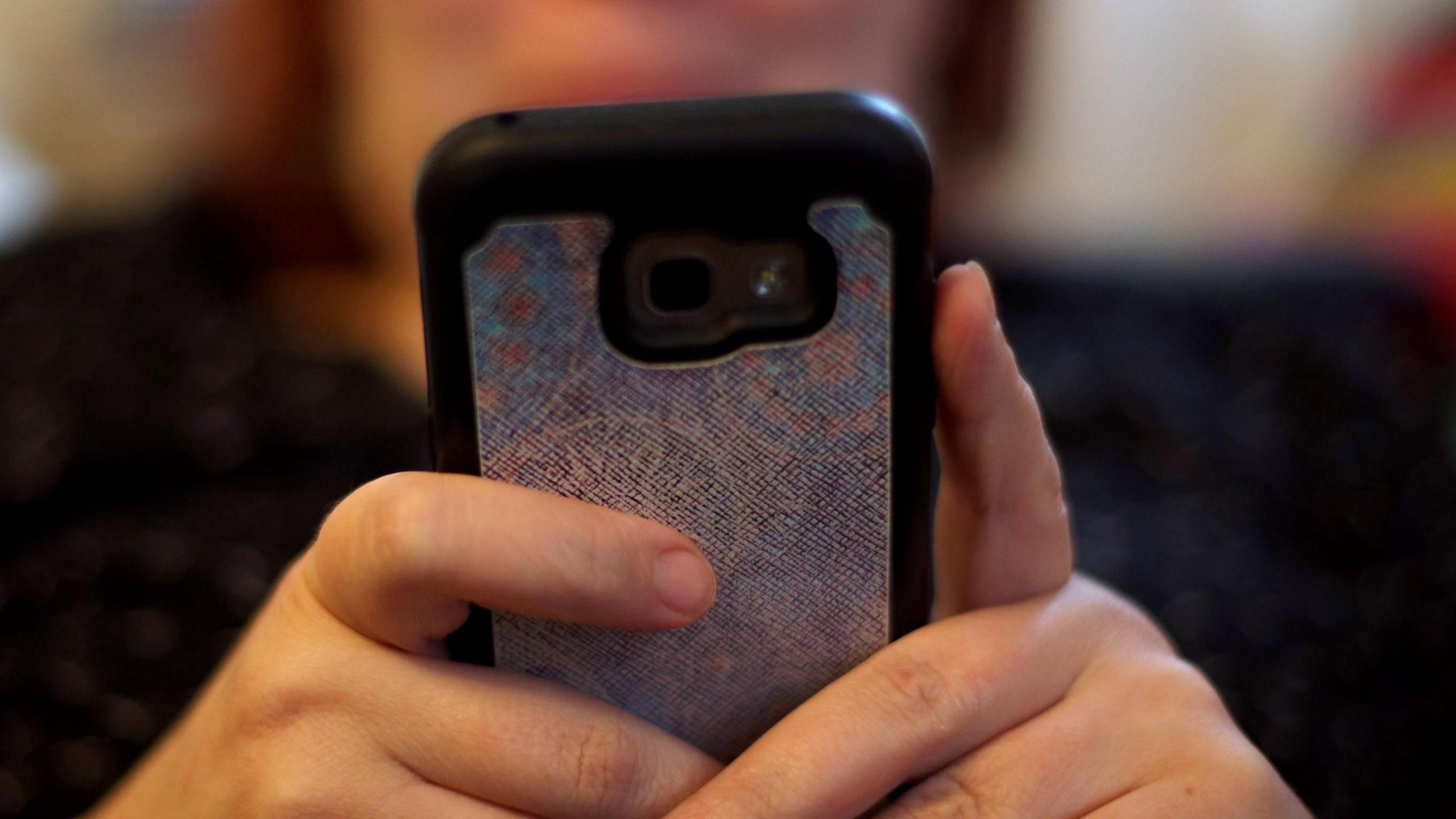 Generic close-up image of a woman holding her mobile phone in front of her. It has a shiny silver cover.