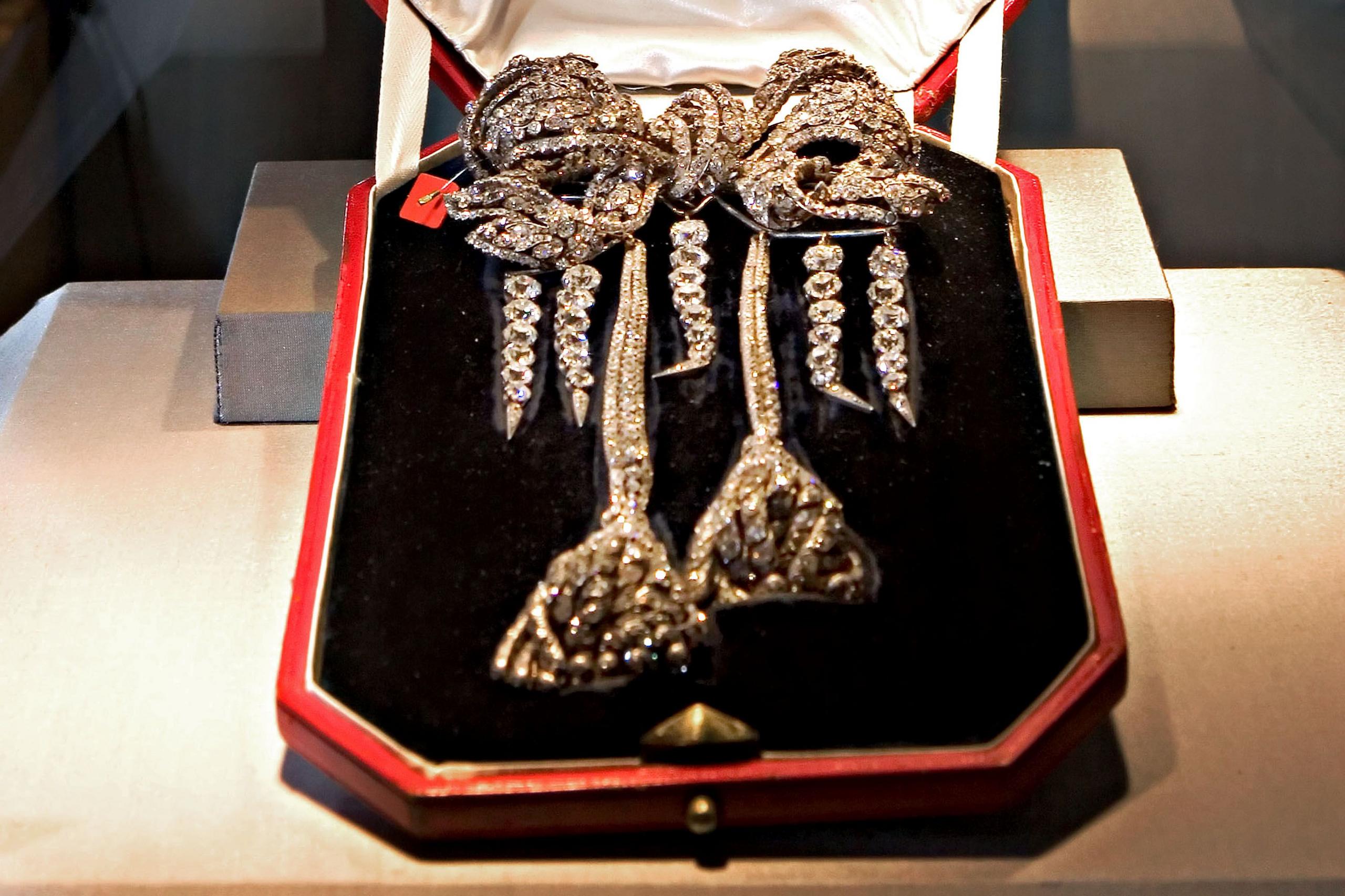 The antique Empress Eugenie Brooch, an antique diamond bow brooch, pictured in a black velvet box with a red exterior. It is a lavish bow shape with trailing strands of diamonds in the shape of two large tassels, and four further strands hanging from the bow 
