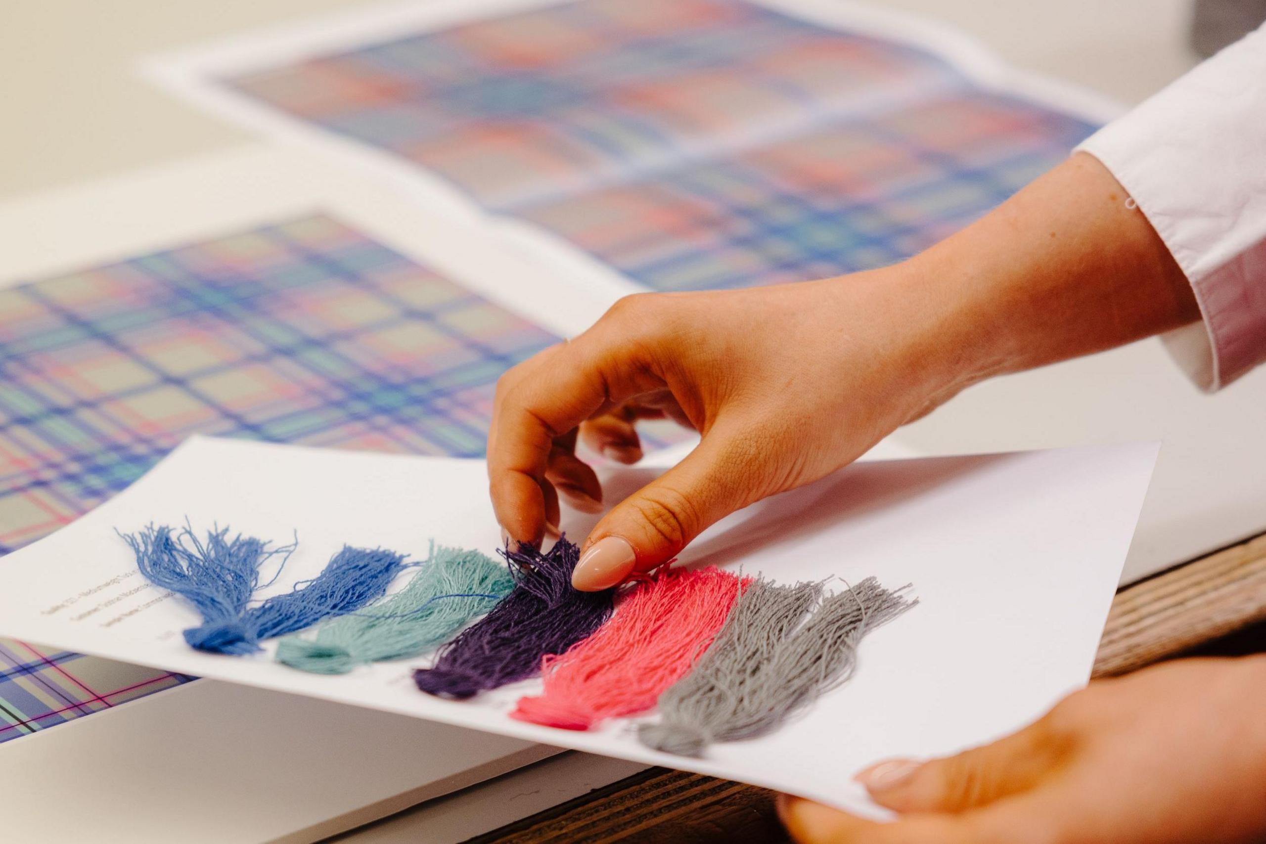 A close up of the designer's hands, touching the thread swatches over the tartan design.