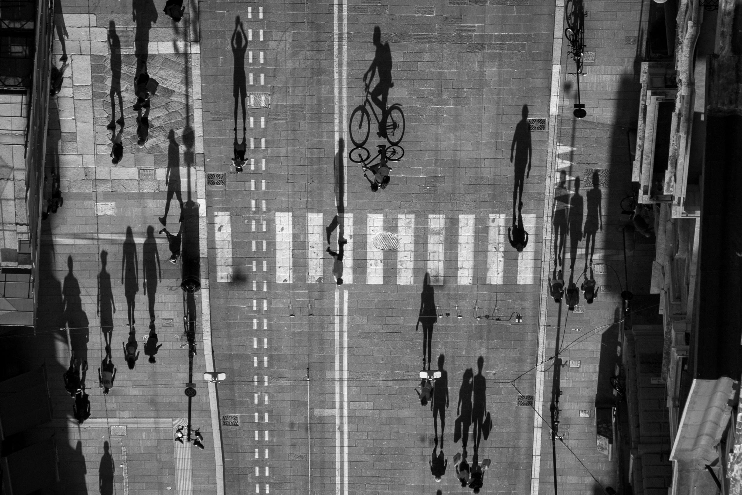 A street seen from above as people cast long shadows on the ground