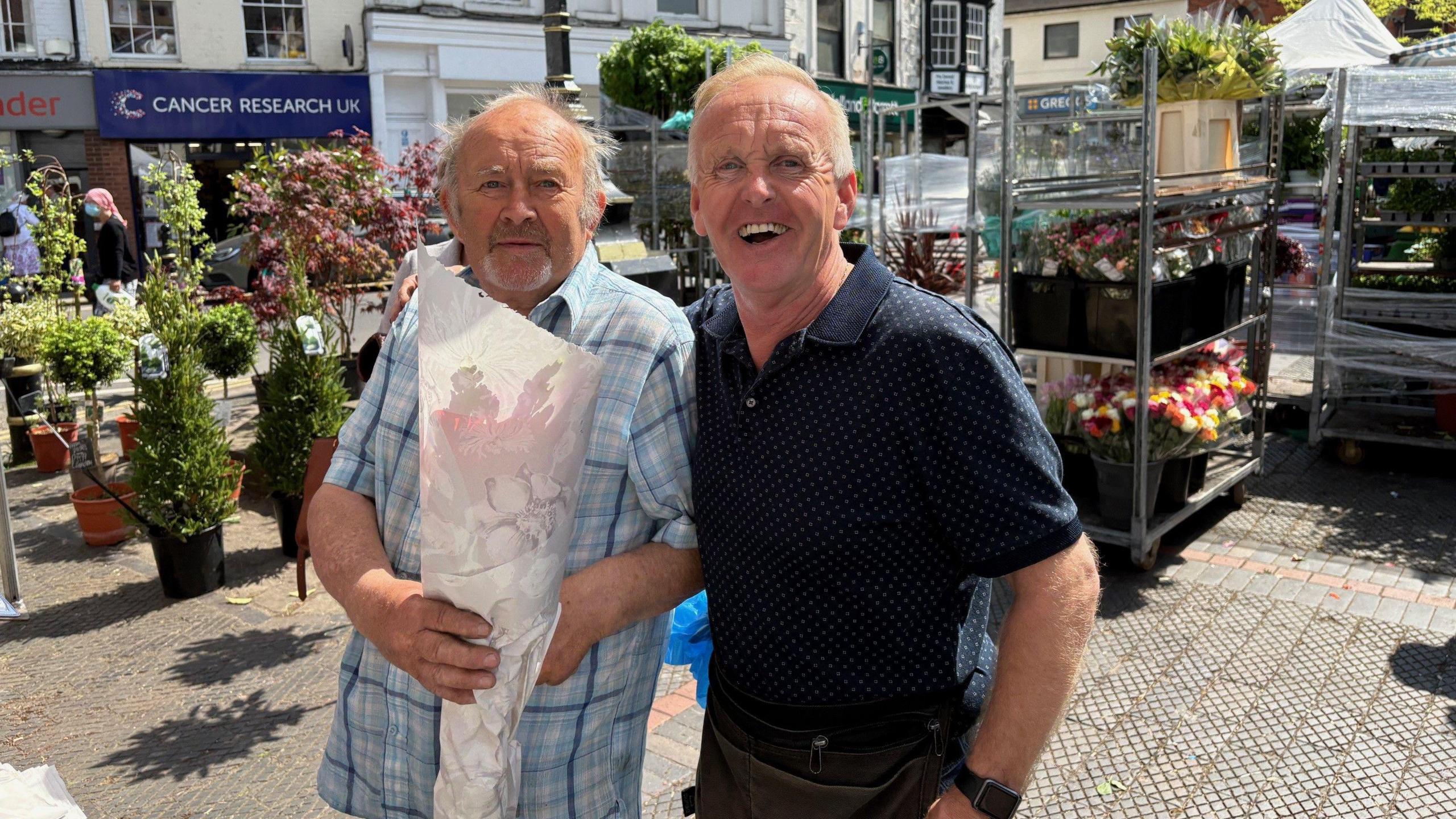 Two men, including Andrew Dennis, on a market stall. The other man is holding a bouquet of flowers
