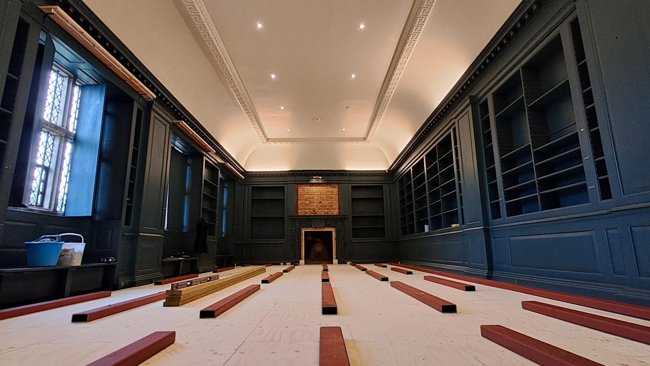 Image of Avebury Manor West Library interior with wooden planks on the floor, ready for renovation, and dark blue book cases around the edge of the room. 