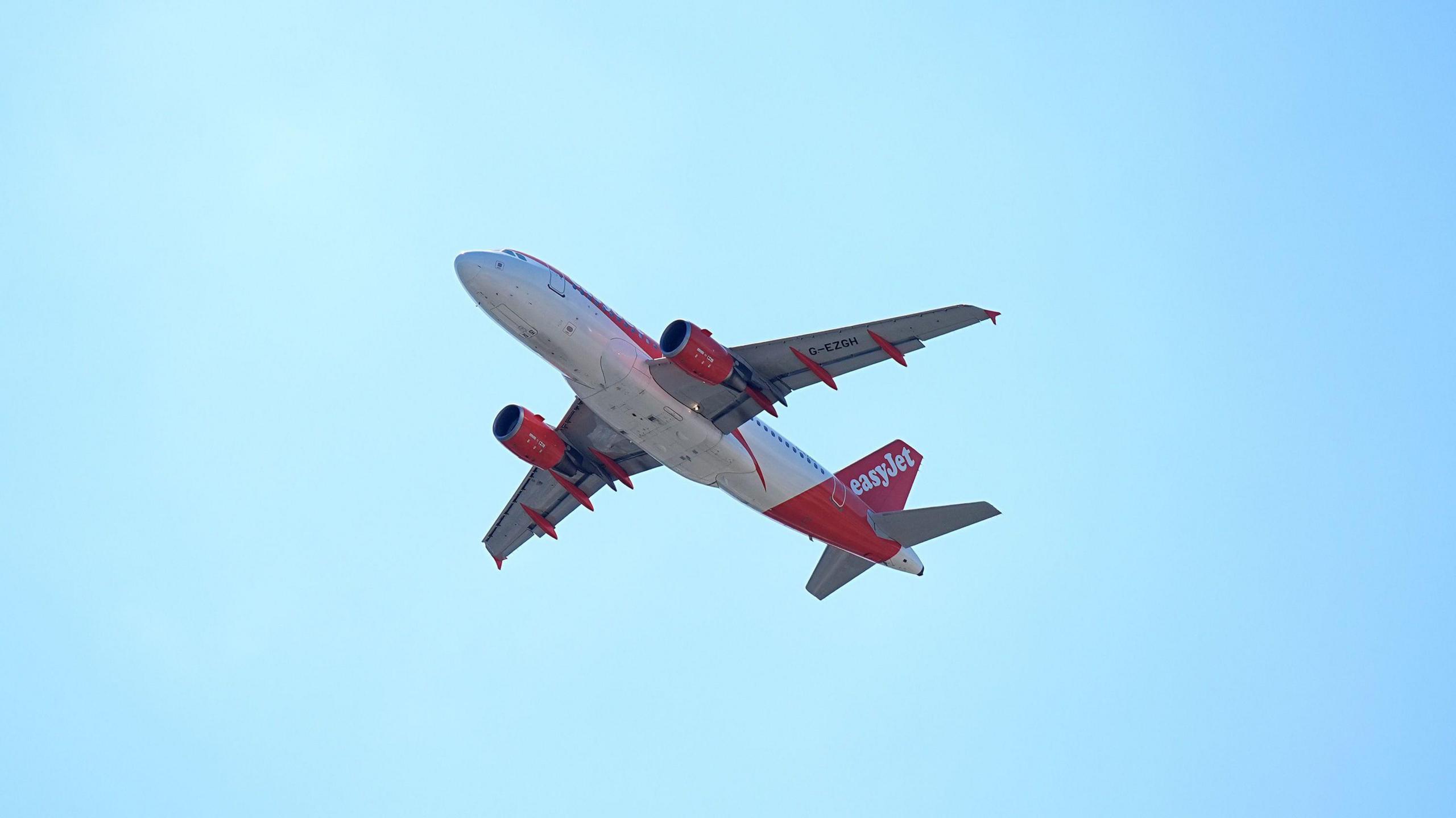 A plane takes off. It is flying high in a clear, pale-blue sky.