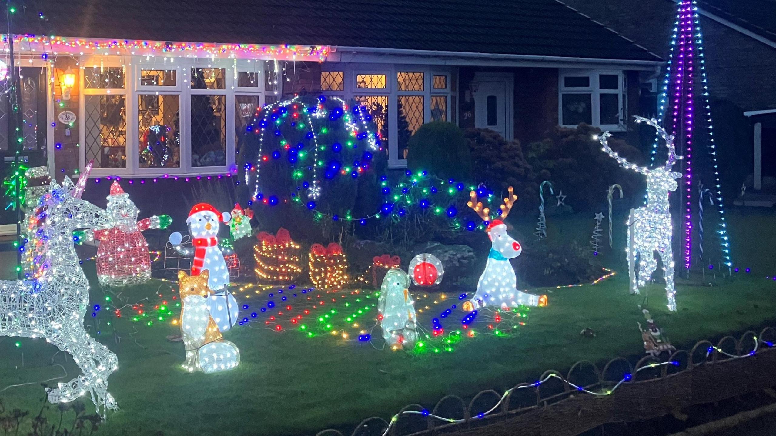 A front garden of a home on Warwick Street, filled with illuminated Christmas figures, including a unicorn, fox, snowmen, penguin and reindeer. Each is lit up white, red, blue, and green.