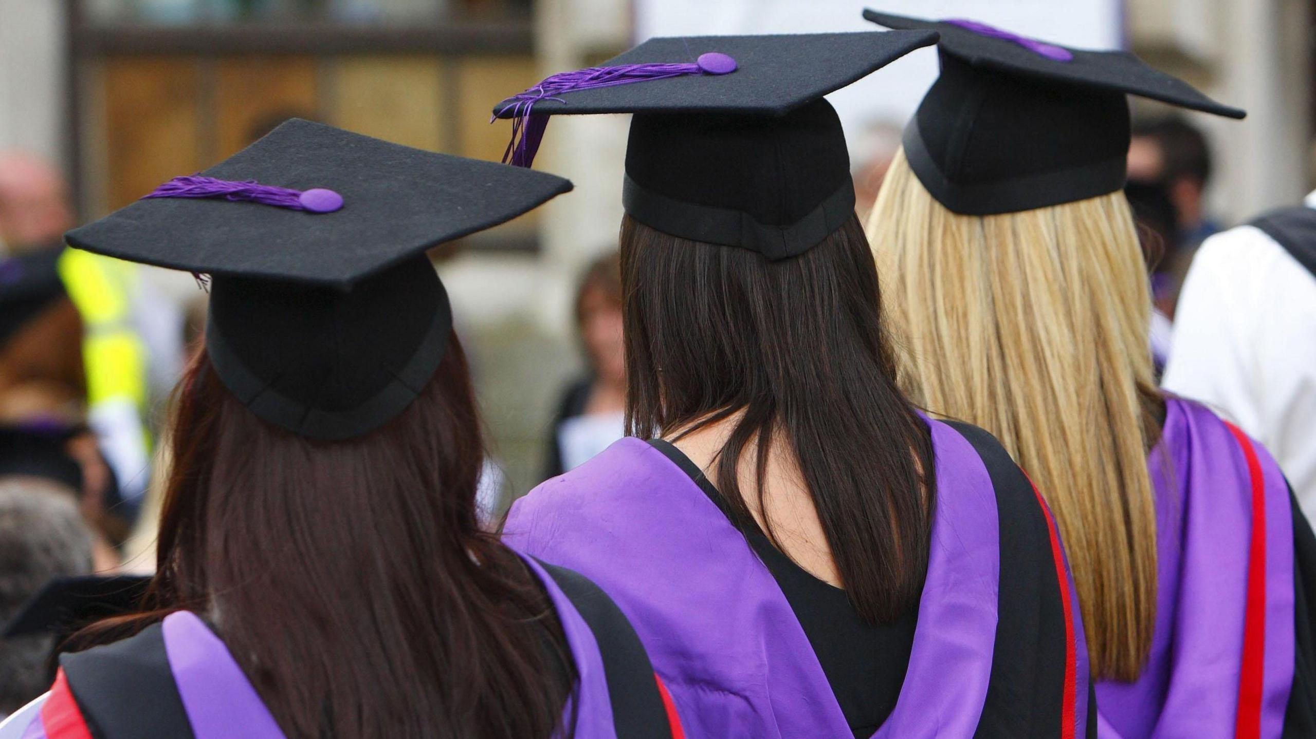 A photo from behind of three female university students wearing graduation caps and gowns.