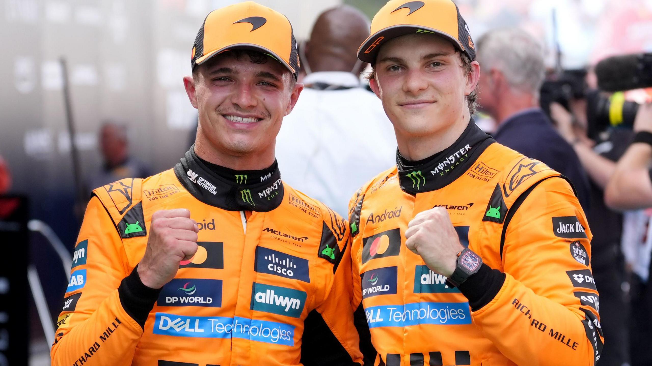 McLaren team-mates Lando Norris and Oscar Piastri smile and each hold up one clenched fist in celebration after finishing first and second in the Spanish Grand Prix