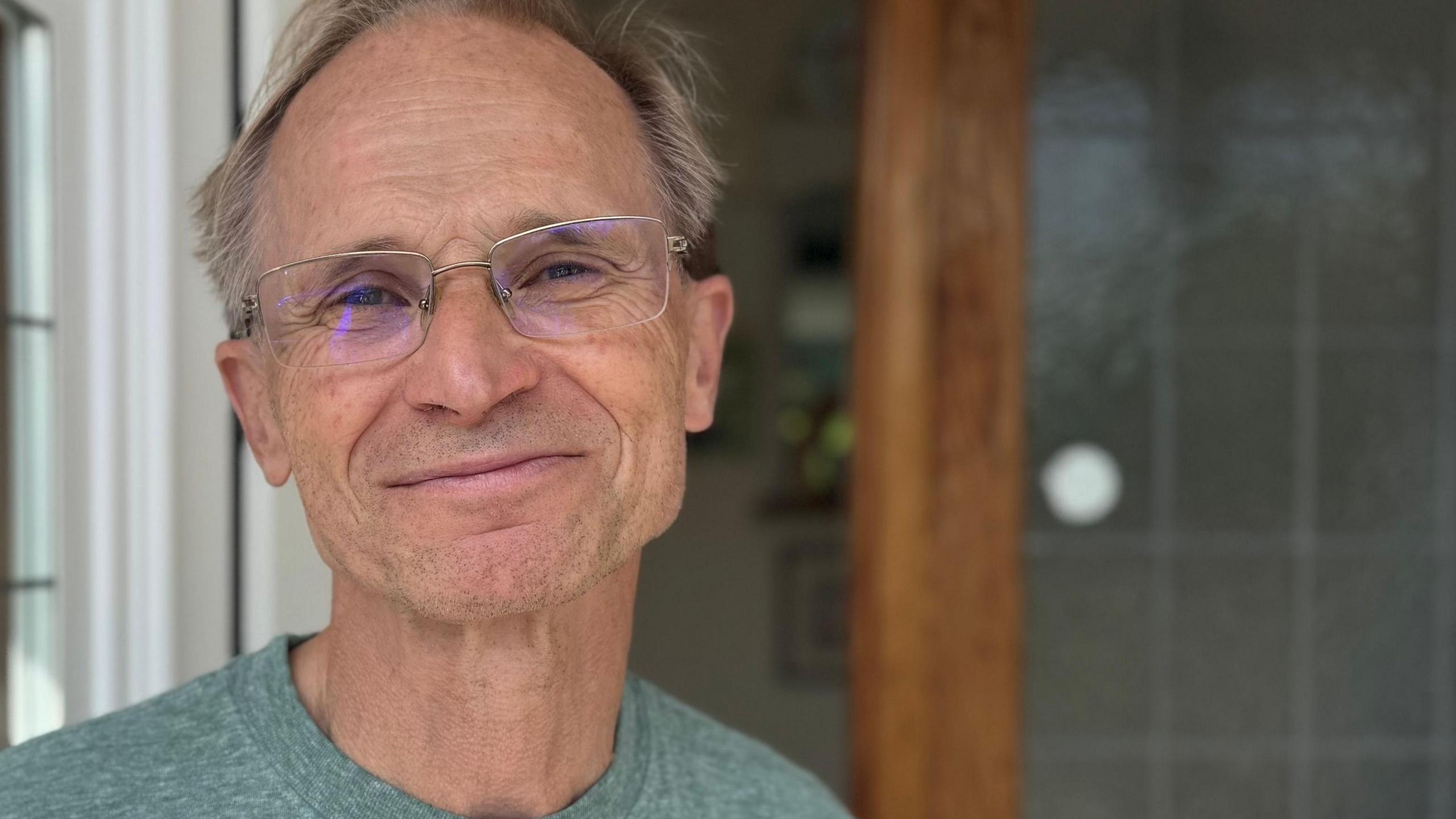 The head and shoulders of Tim Lockington. He is wearing a grey T-shirt and glasses and looking into the camera. He appears to be standing in a doorway.