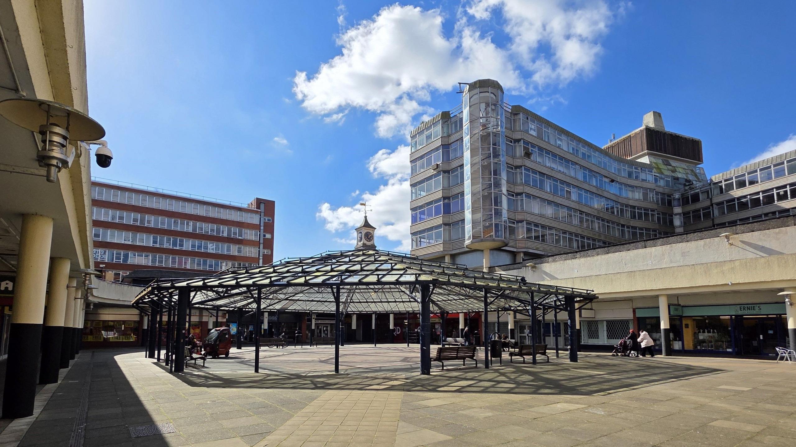 A concrete shopping precinct is built around a glass-roofed circular veranda with office blocks towering high over it on either side.