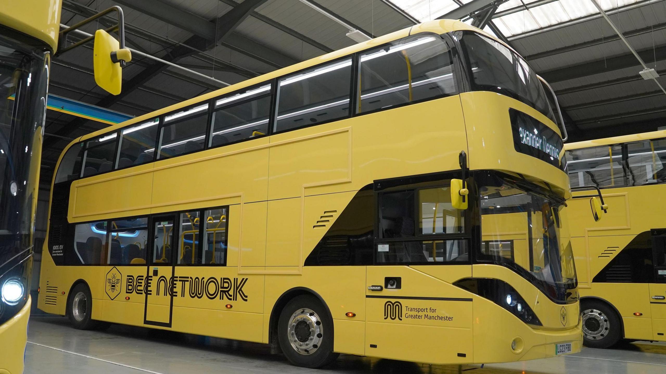 A line of three parked yellow buses in a manufacturing depot