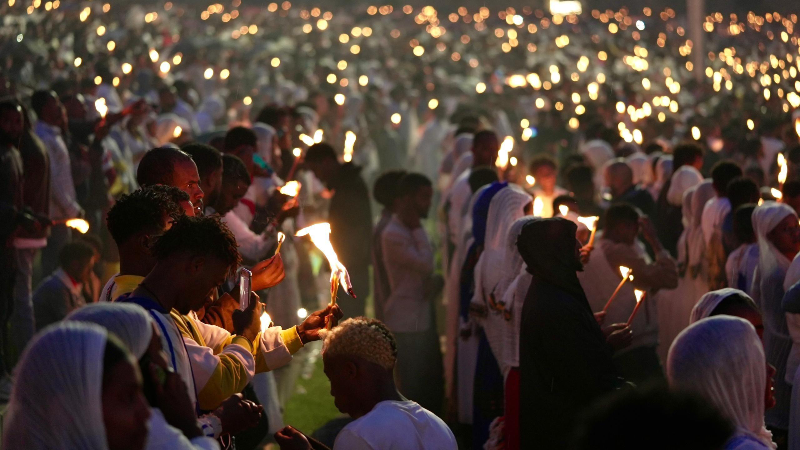 A crowd of worshippers hold lit torches