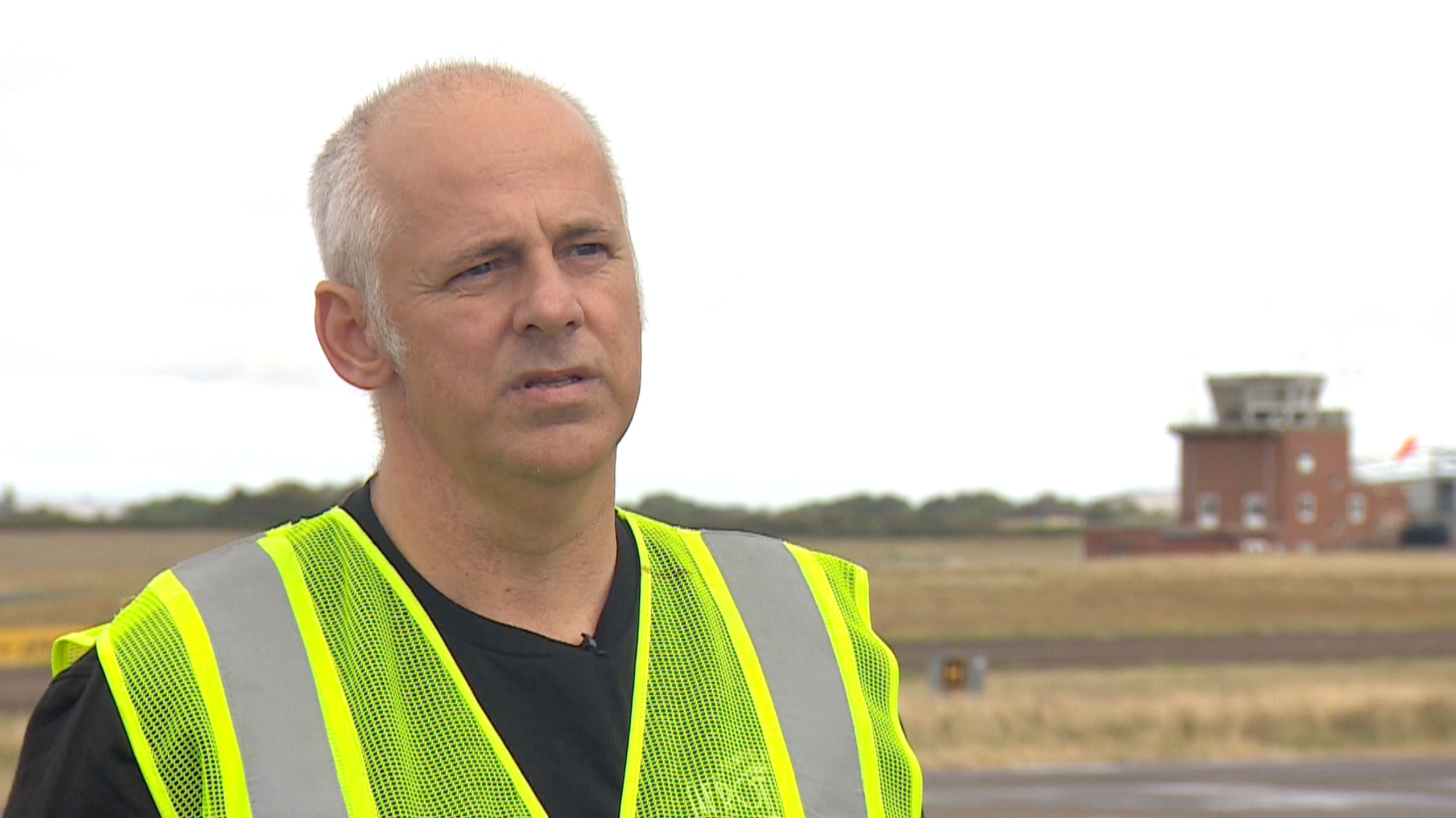 Darren Lewington at Gloucestershire Airport. He is wearing a fluorescent yellow jacket over a black t-shirt.
