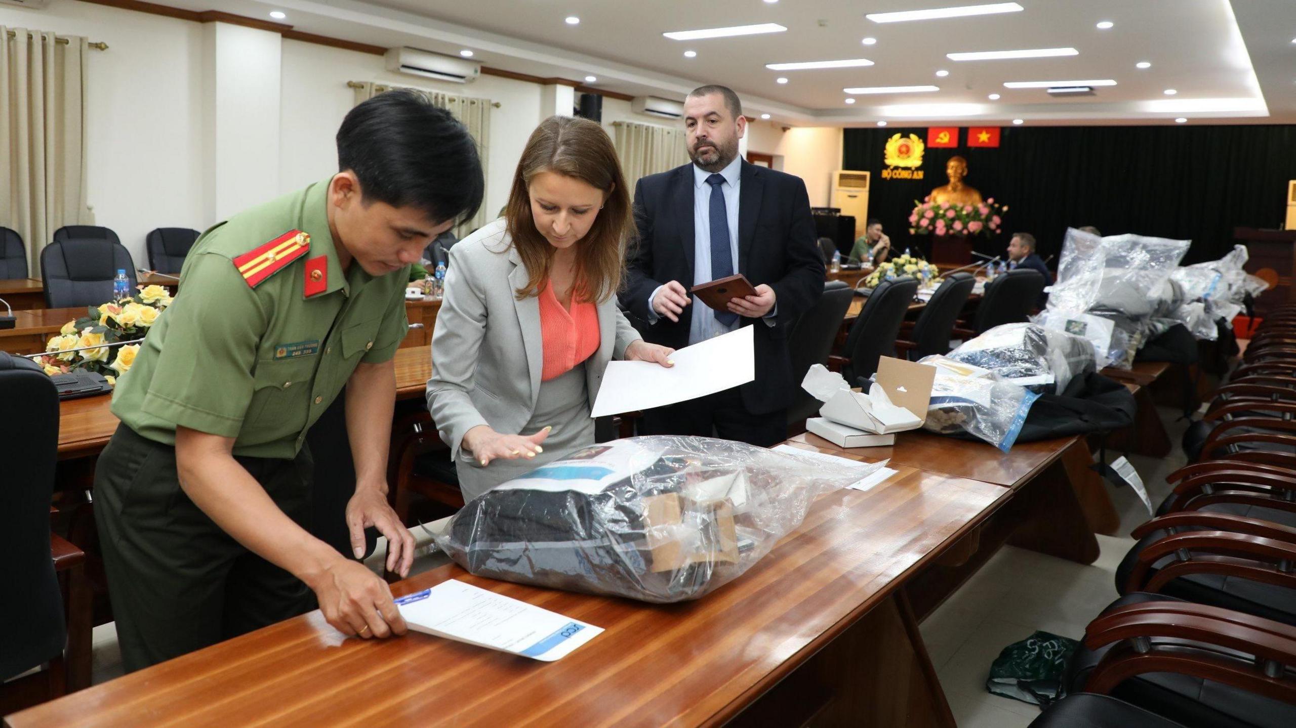 Police officers hand over bags of possessions, which are on a long wooden table, to a Vietnamese official. 