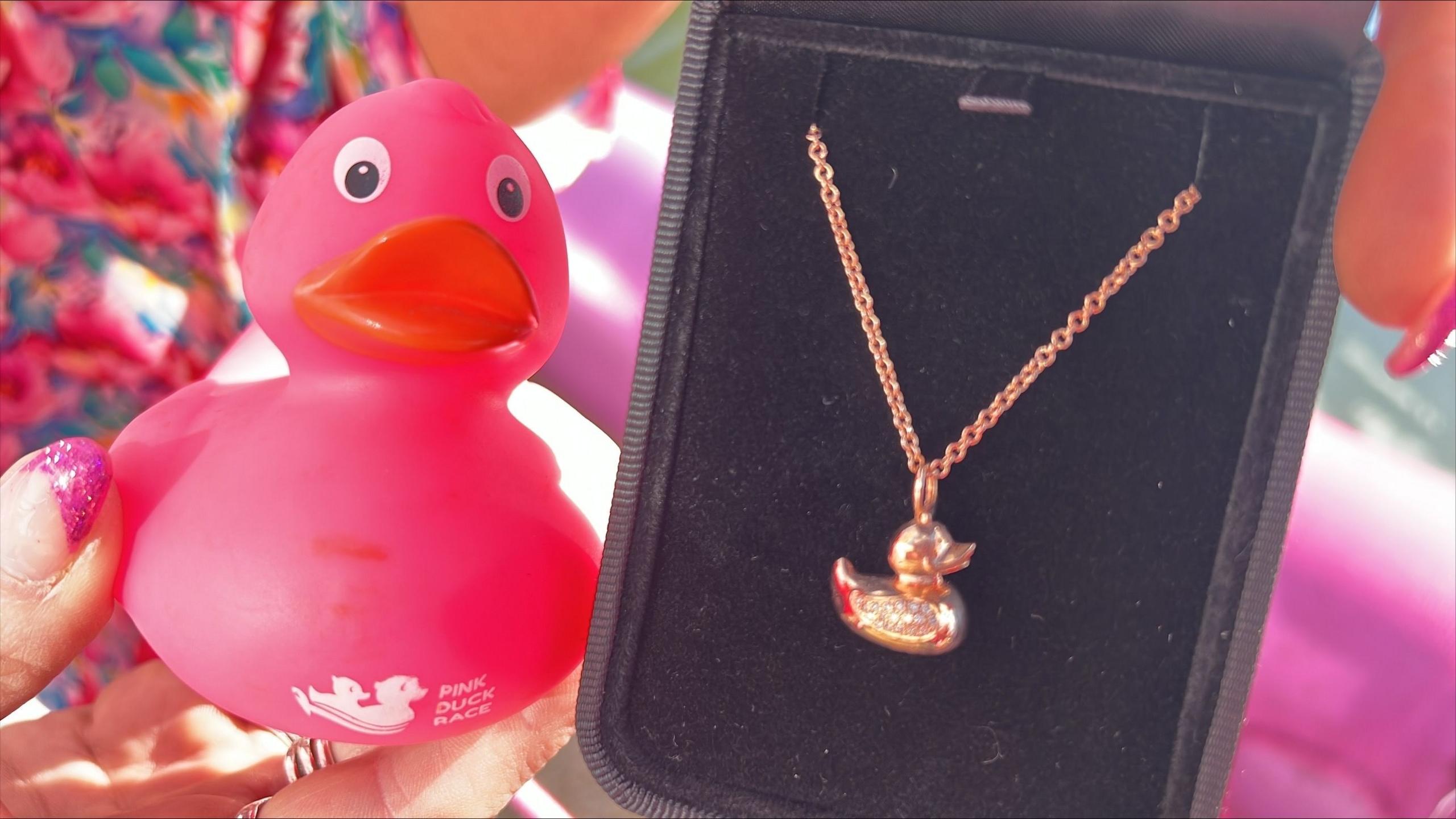 A pink duck being held next to a gold necklace designed to look similar and encrusted with diamonds on its wing.