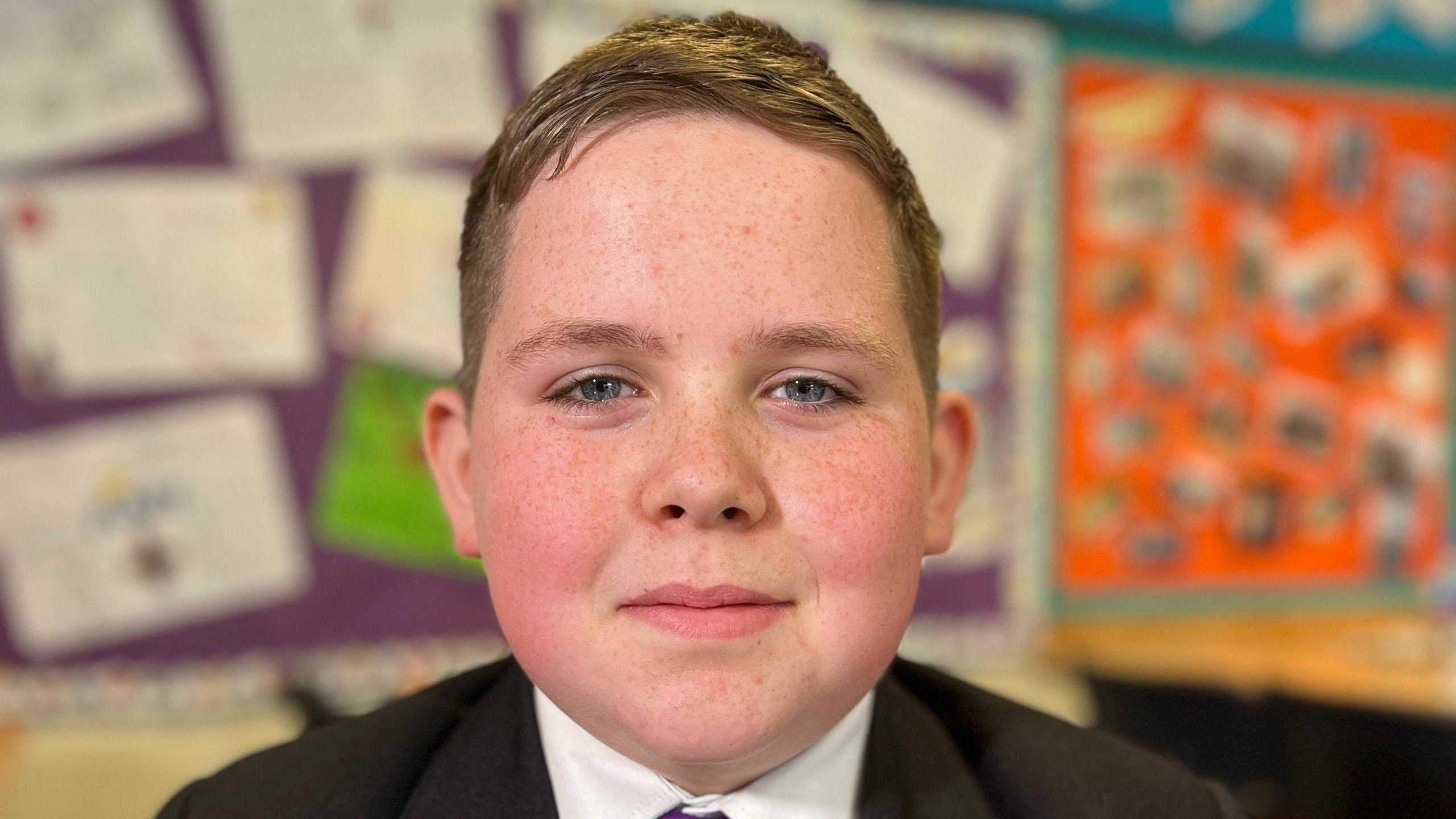 Carson, wearing his uniform smiles at the camea in the classroom