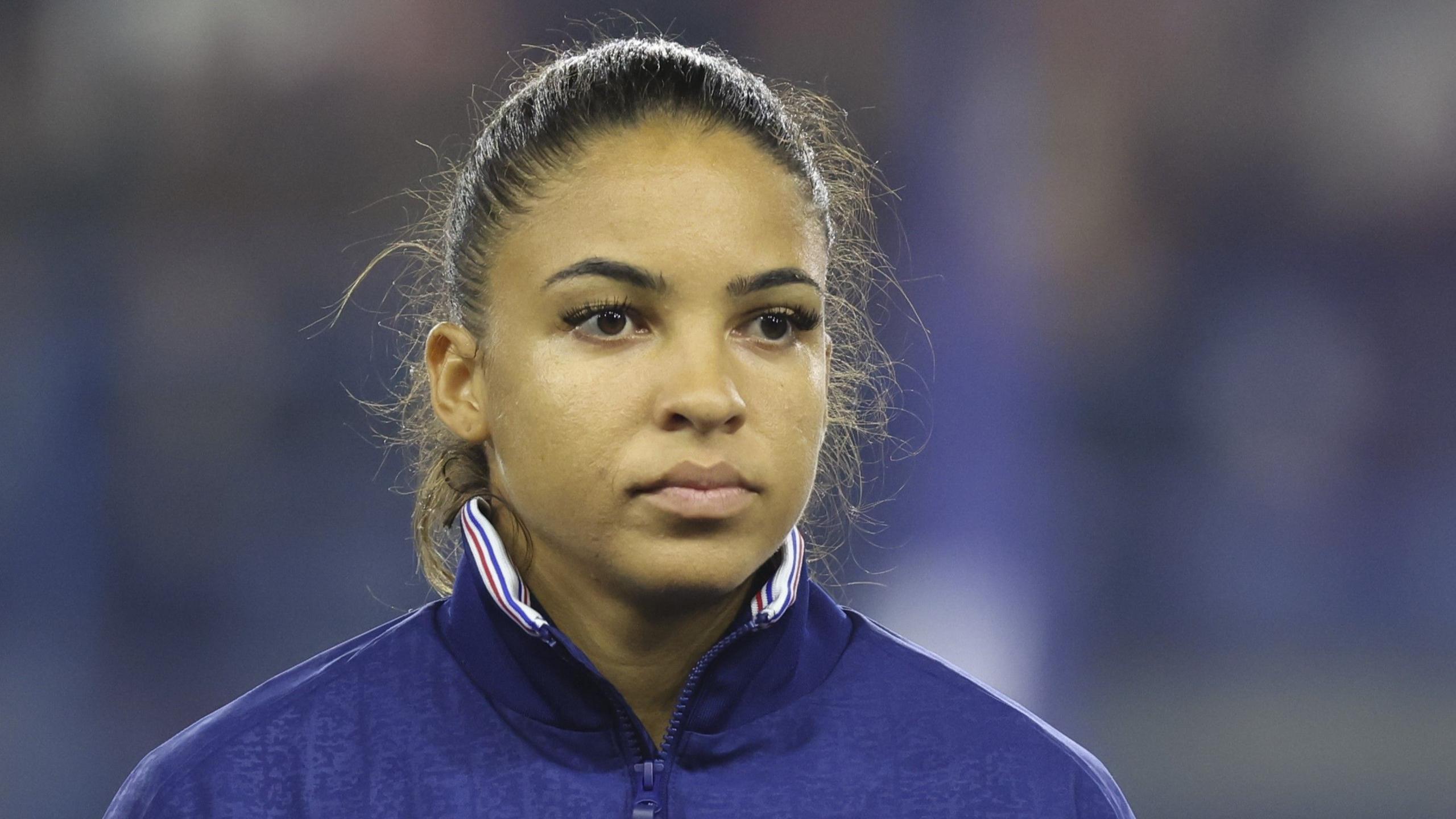 Delphine Cascarino watches on, wearing a tracksuit top, before a France international