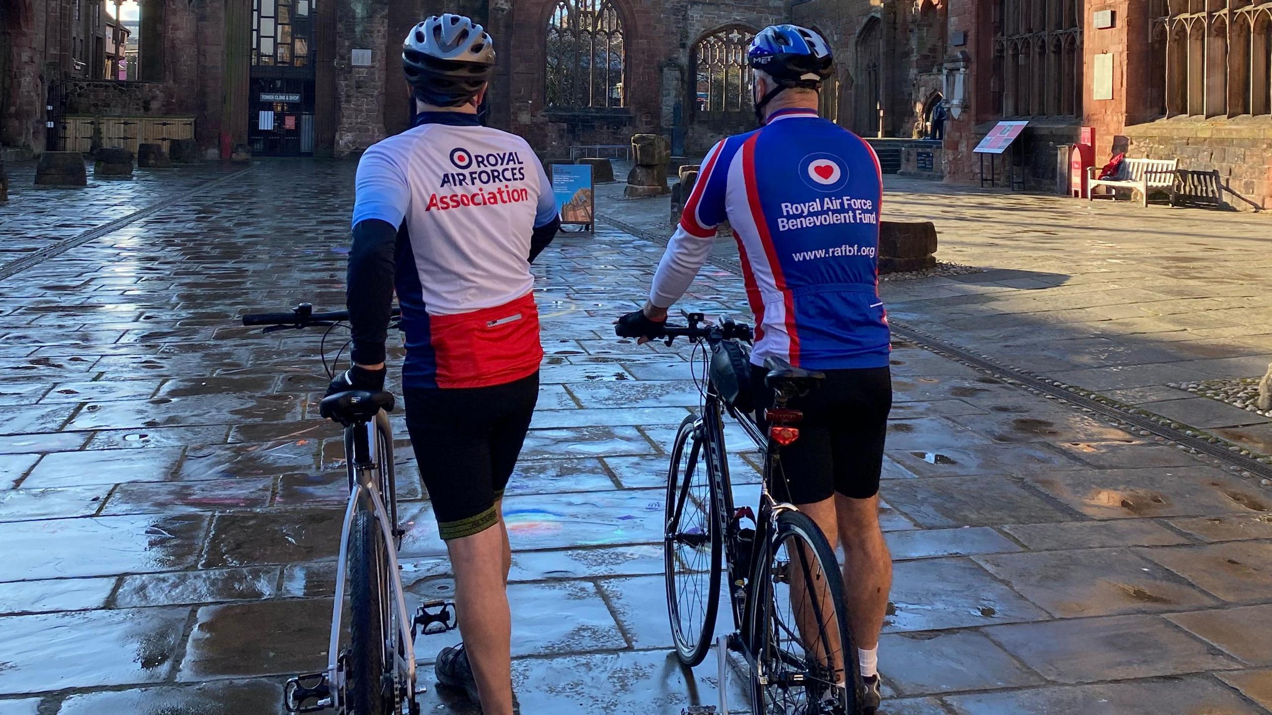 Stuart and Roger are with their bikes again, this time we are seeing them from behind. They are to the side of their bikes, looking ready to climb back on and get going.