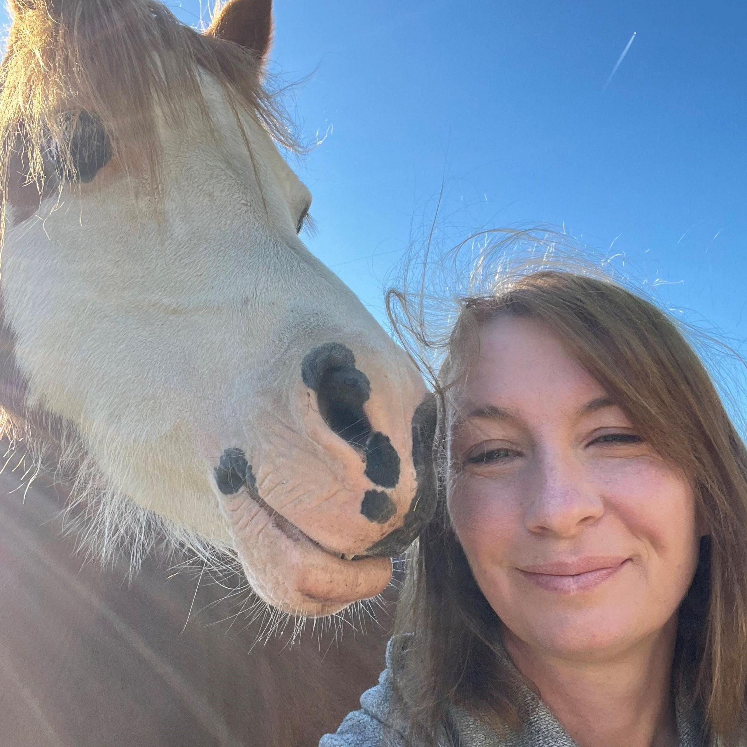 A woman with long light brown hair smiling in a selfie with a brown and white pony