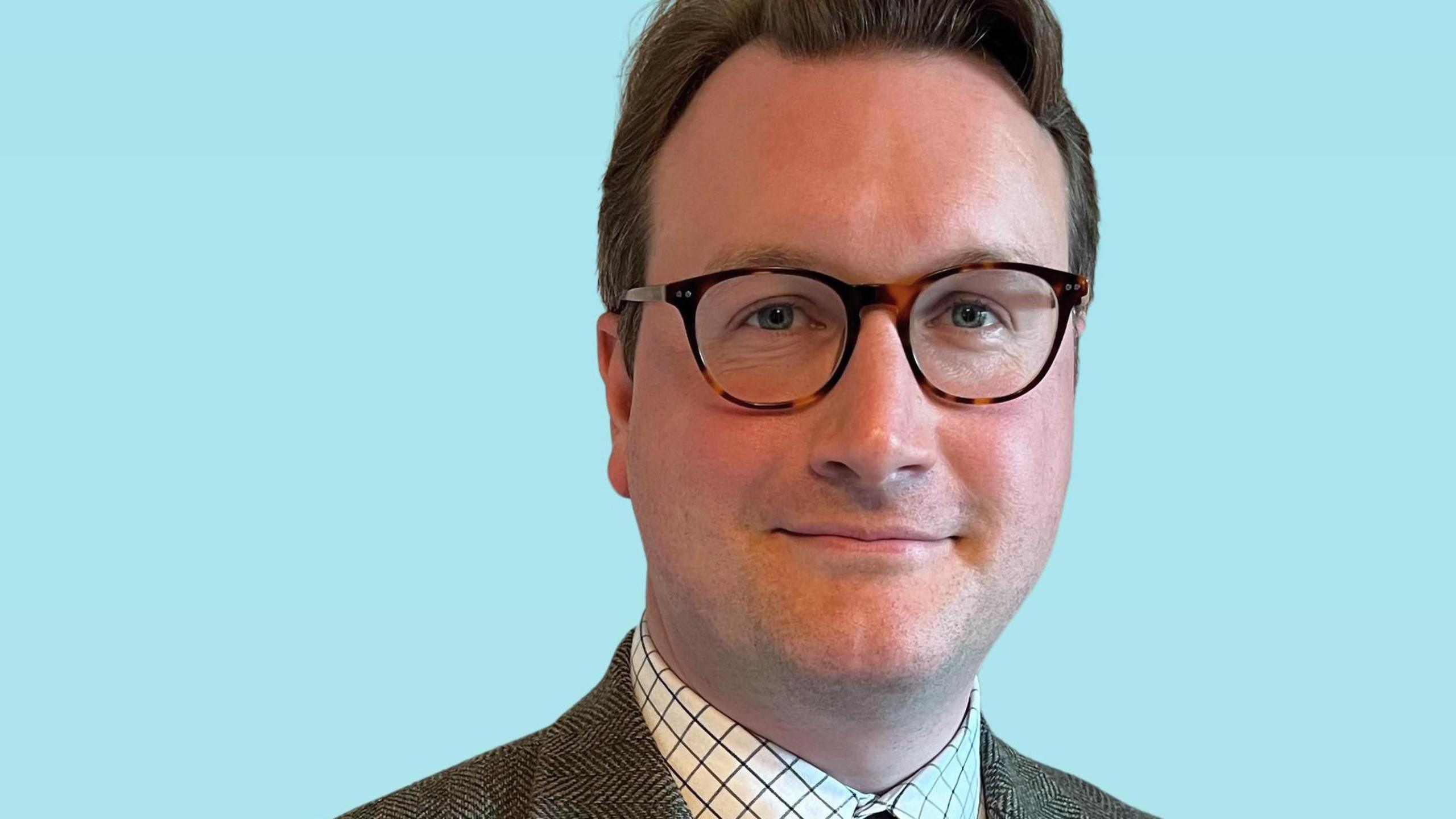 David Swain in a tweed suit against a blue background.