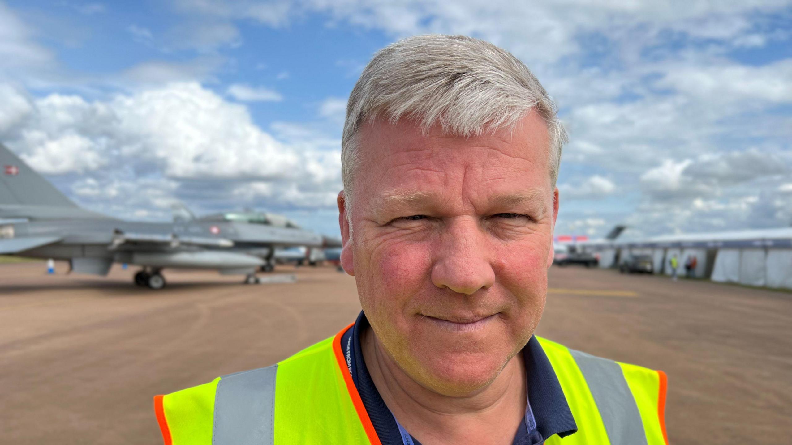 Paul Atherton in a high vis jacket with planes blurred in the background