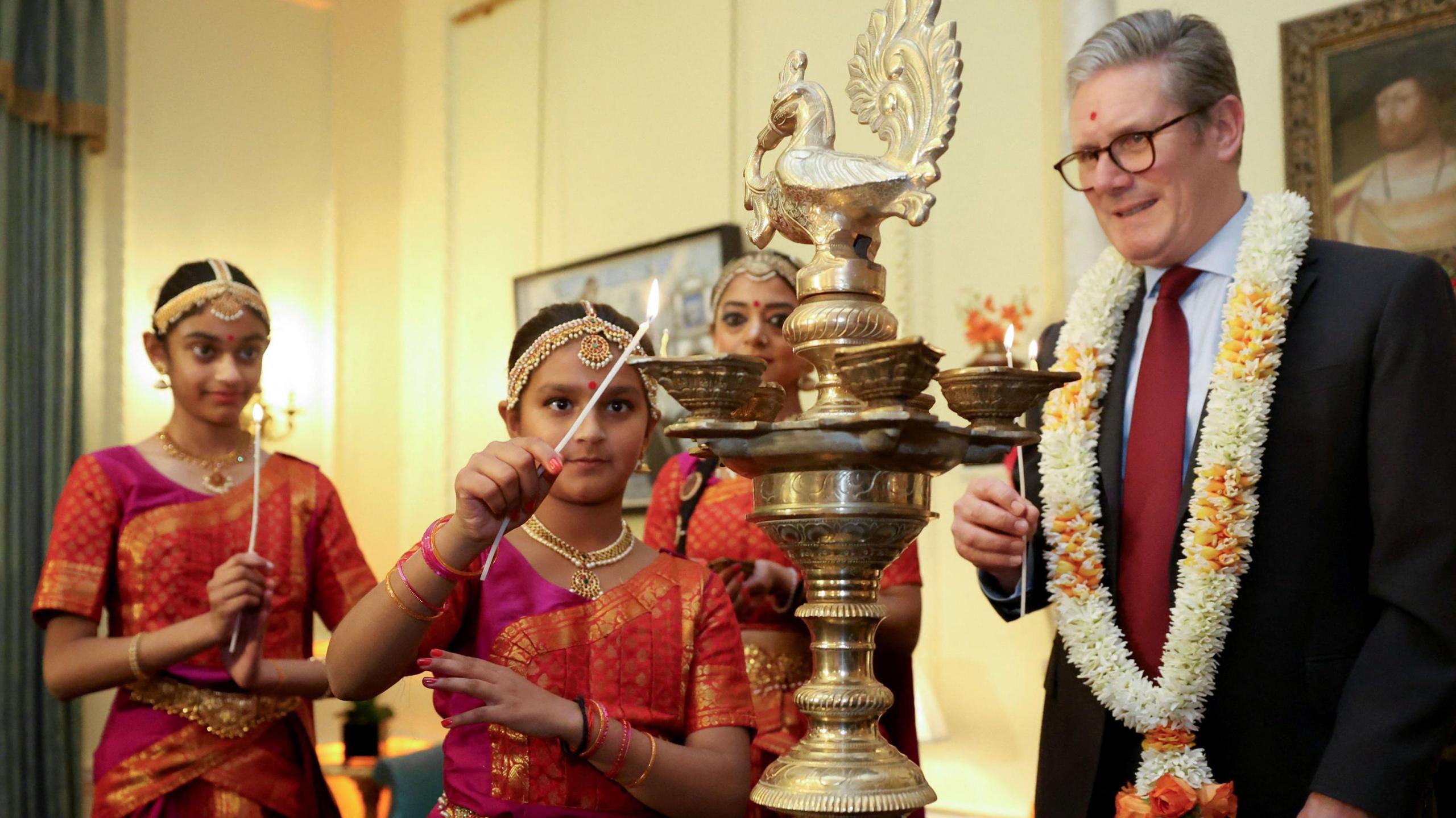 Sir Keir Starmer and members of the Arunima Kumar Dance Company hold candles to light a lamp during a reception to mark Diwali