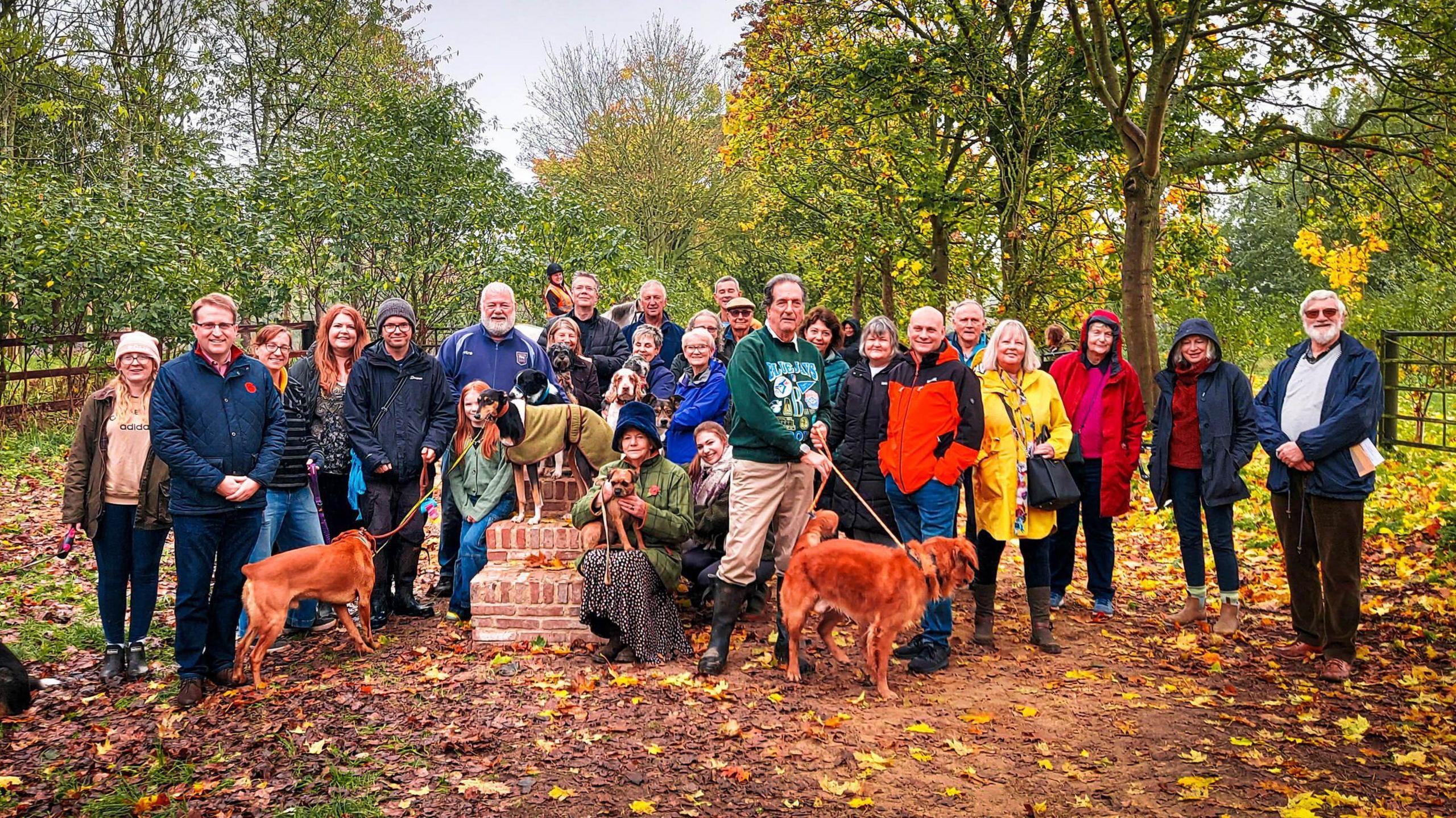 Councillors and residents, including some with dogs, gathered together in a woodland area.