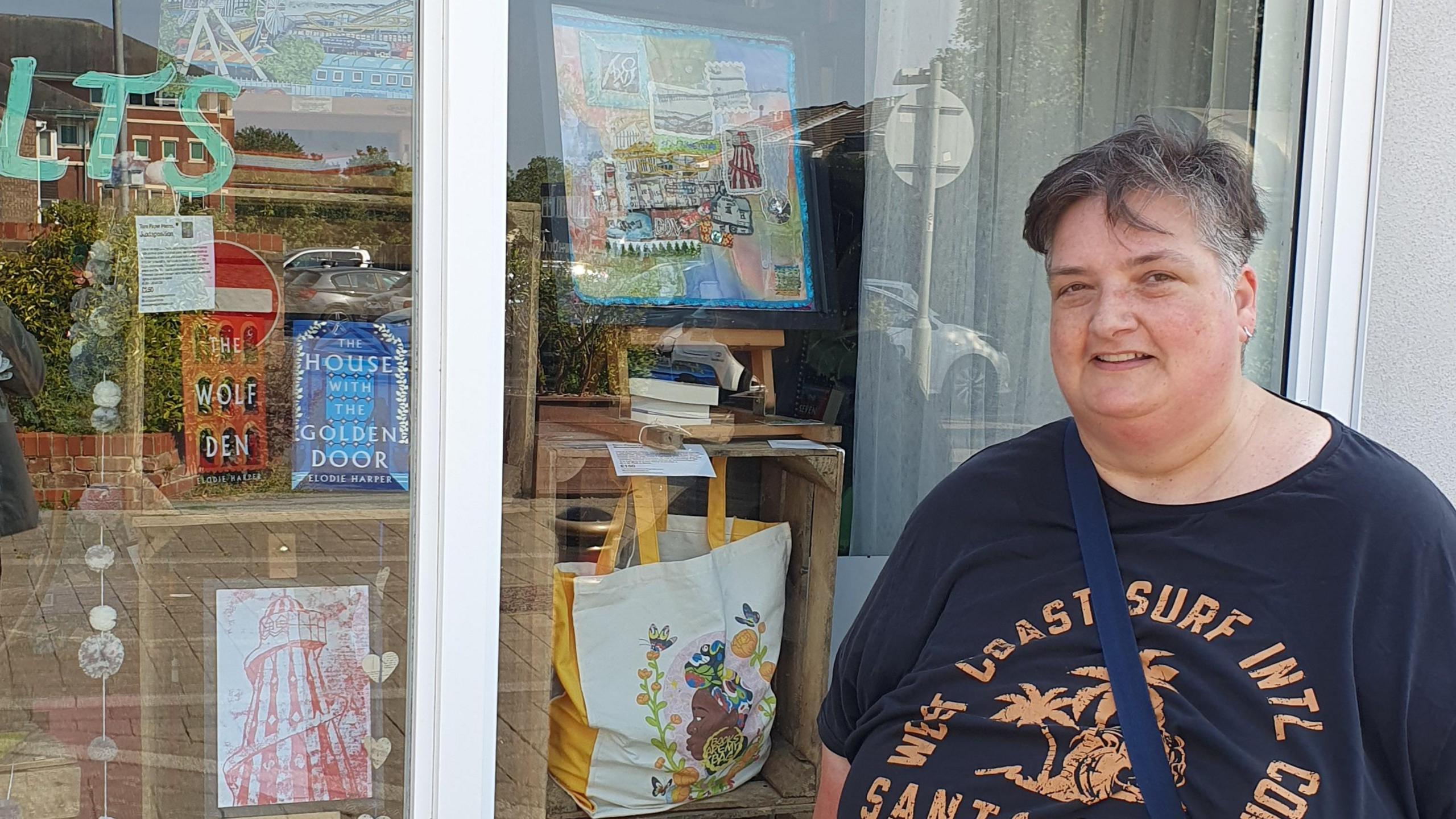 Allie Watson standing in front of a shop window, which has art and books in it.